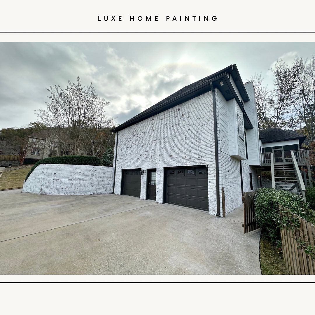 A white house with two garage doors and a driveway in front of it.