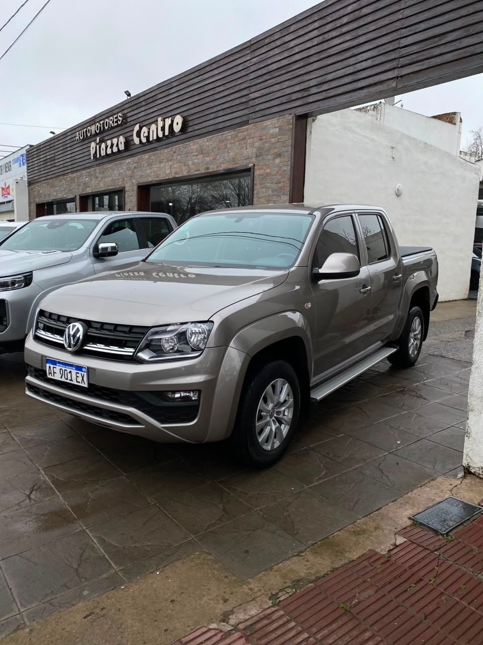 Camioneta Volkswagen gris estacionada frente a un concesionario en una calle mojada.