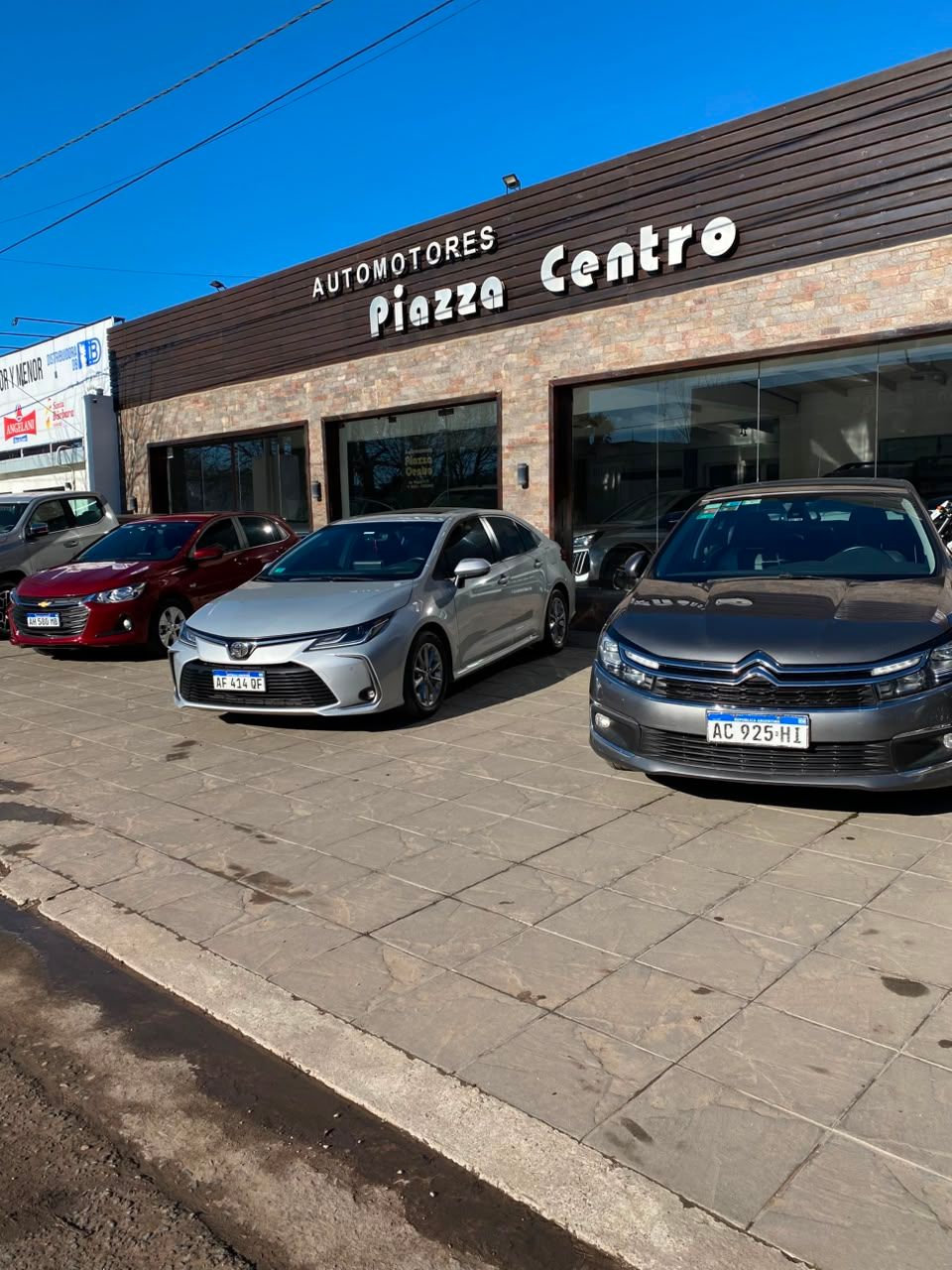 Exterior de un concesionario de automóviles con varios coches aparcados frente al edificio de la sala de exposición.