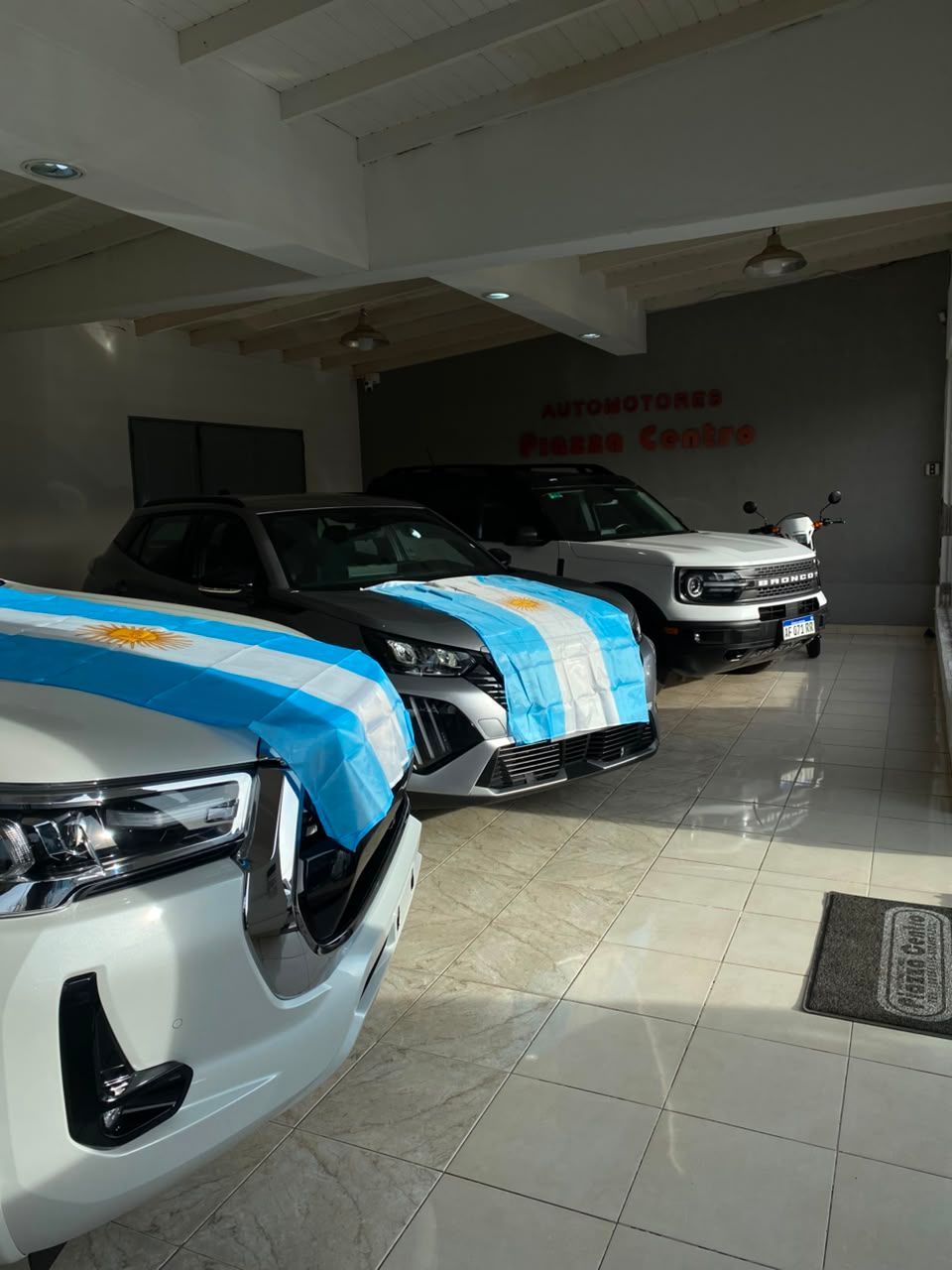Automóviles cubiertos con lonas protectoras de rayas azules, alineados en el interior de una sala de exposición o garaje.
