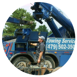 Tow truck driver checking storage compartment on blue truck, sunny day. 