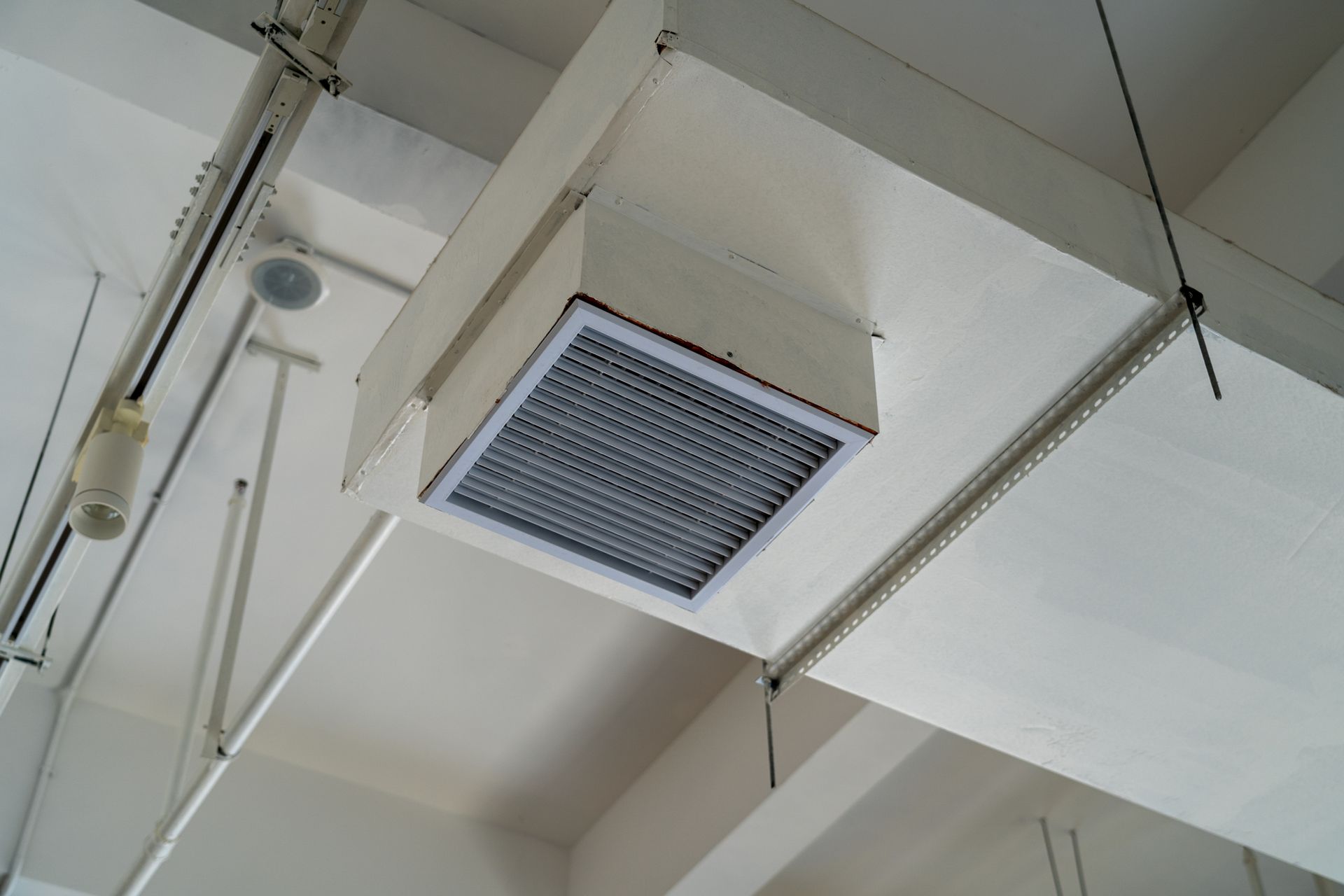 A white air vent is hanging from the ceiling of a building.