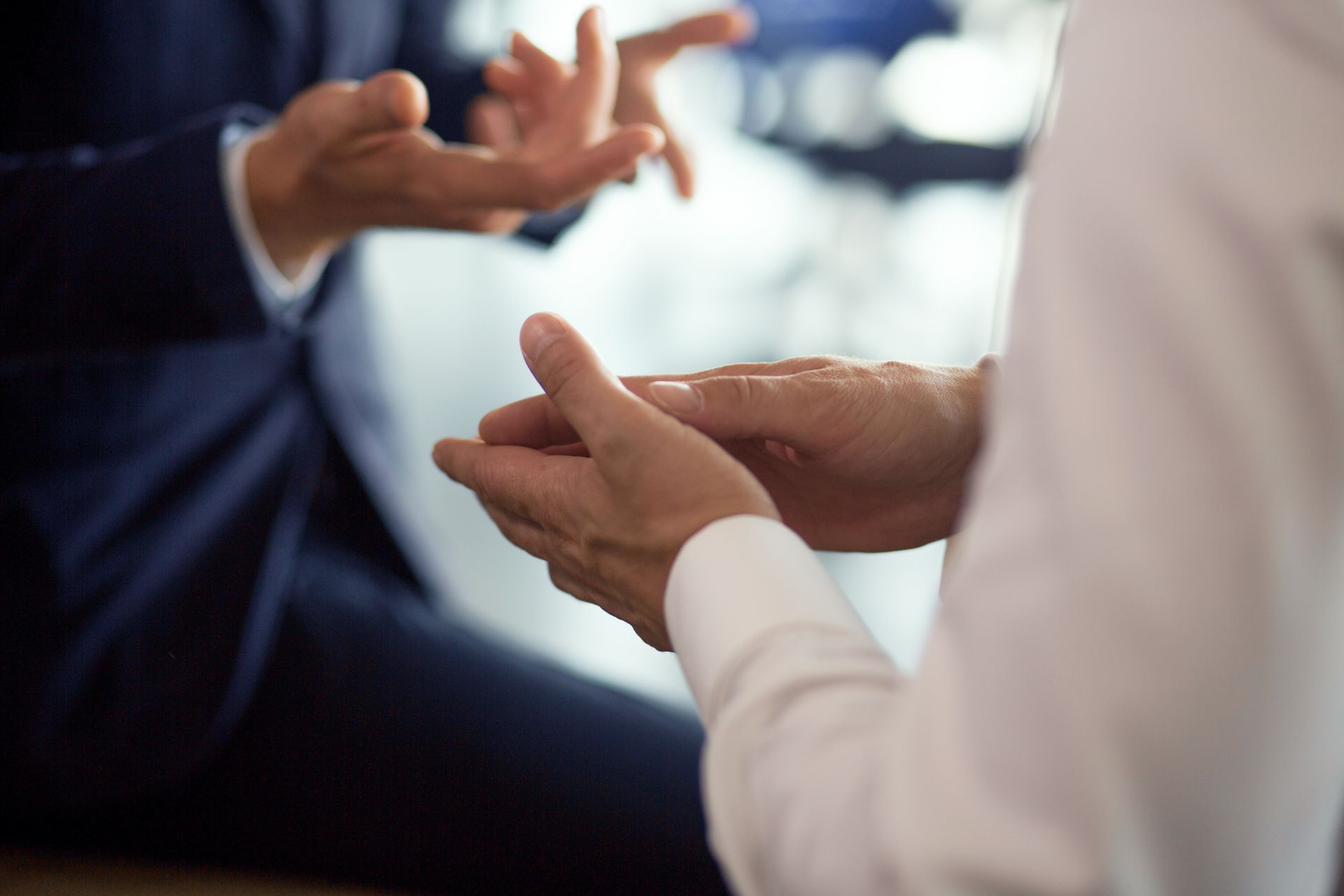 Two people, hands gesturing during a discussion. One wears a suit, the other a white shirt.
