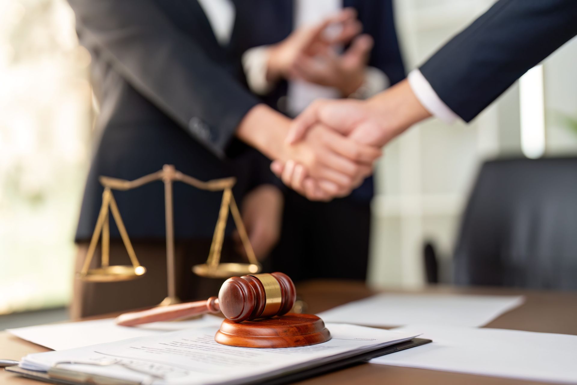 Handshake over legal desk with gavel and scales of justice