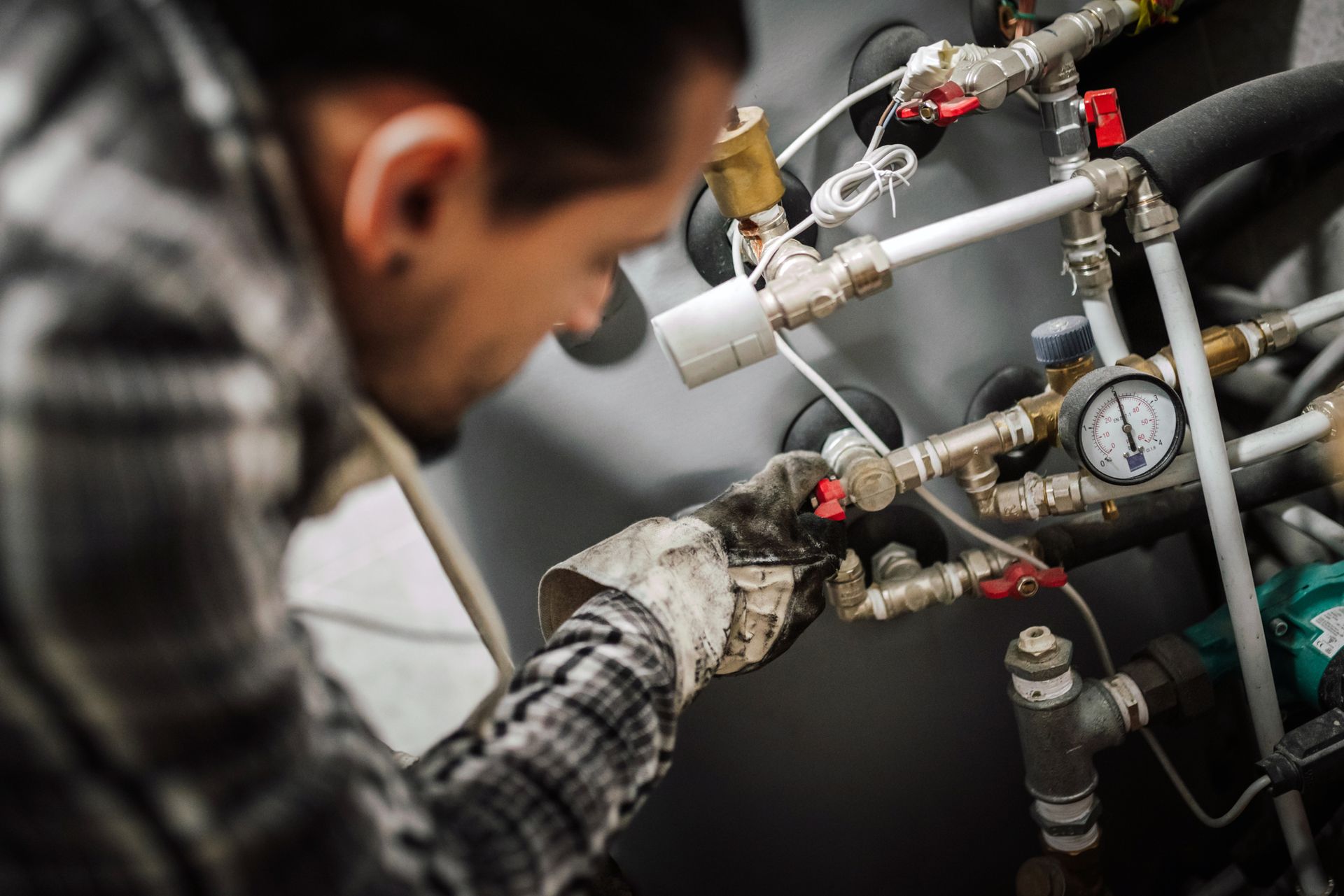 Plumber working on pipes, wearing gloves.  A pressure gauge and various valves are in view.