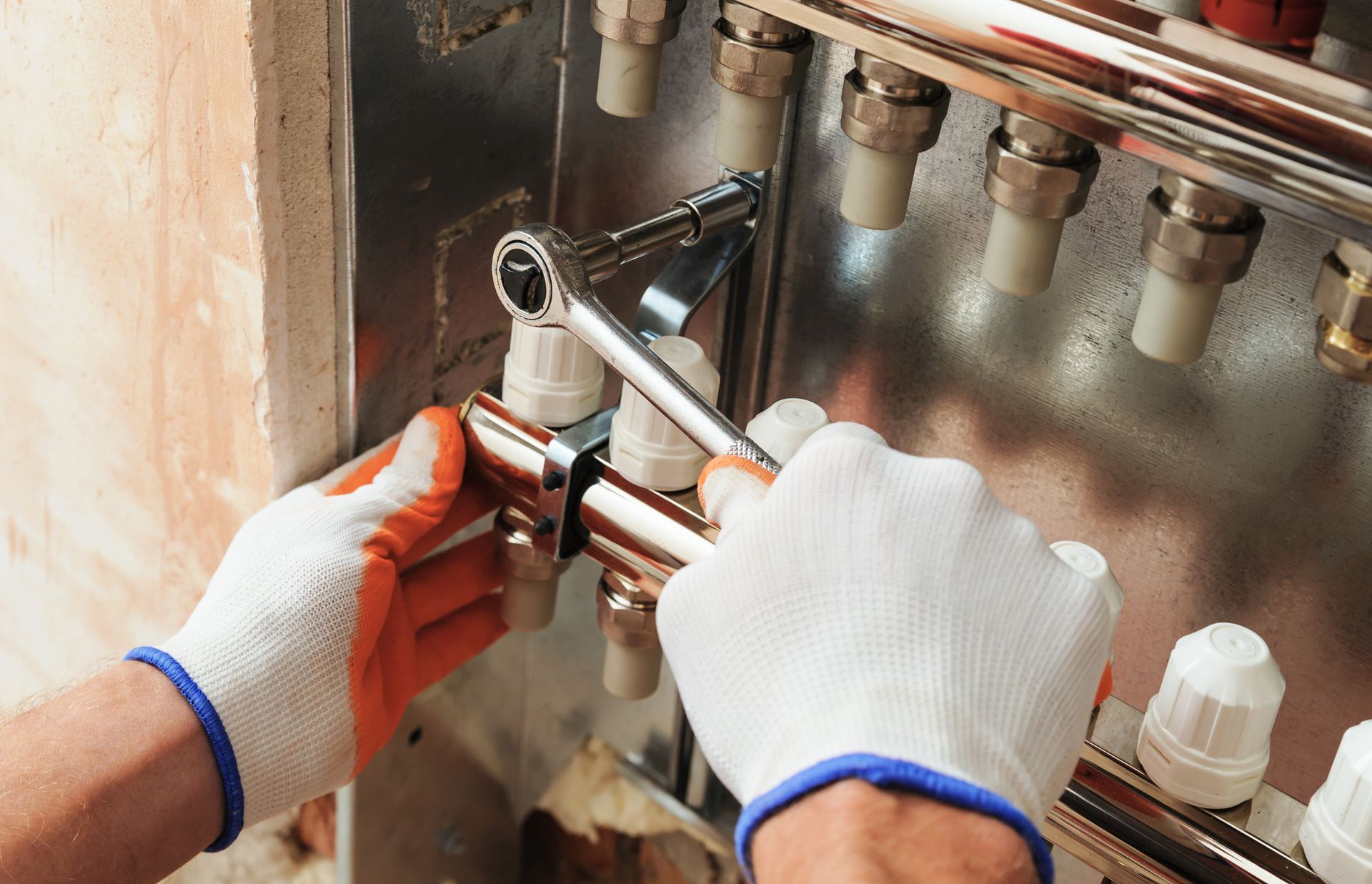 Hands wearing gloves tightening a valve with a wrench on a heating system manifold.