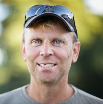 Smiling person wearing sunglasses on a cap against a blurred outdoor background