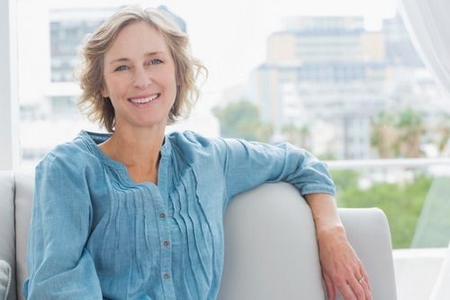Smiling woman in a light blue blouse sitting on a white chair with a blurred outdoor city background