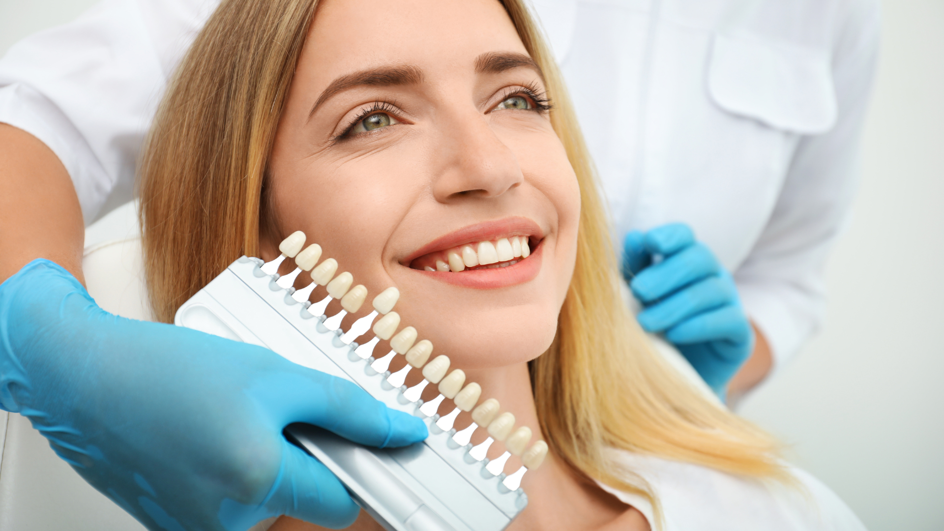 Woman in dentist chair smiles and gives thumbs-up, wearing bib.