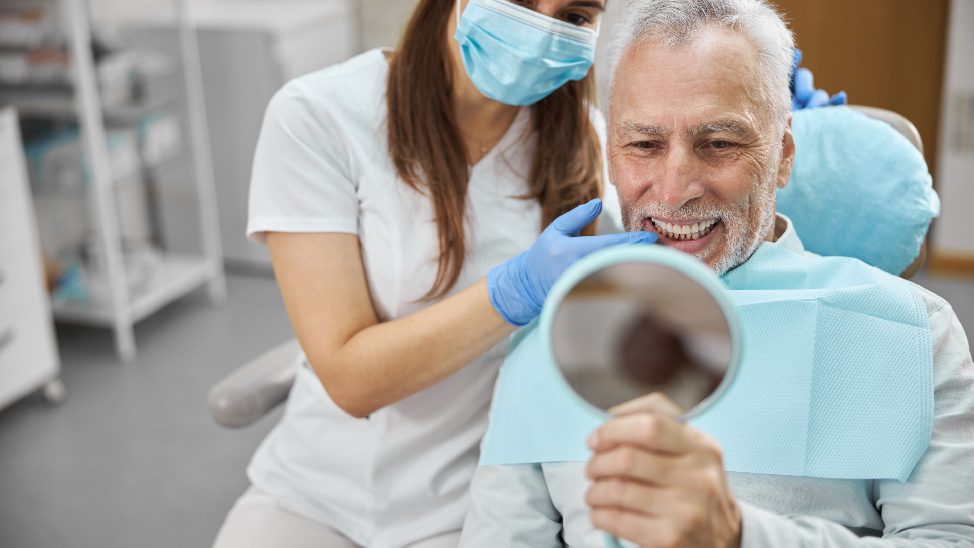 Woman smiling in a dentist chair, looking at a person holding a clipboard, dental tools nearby.