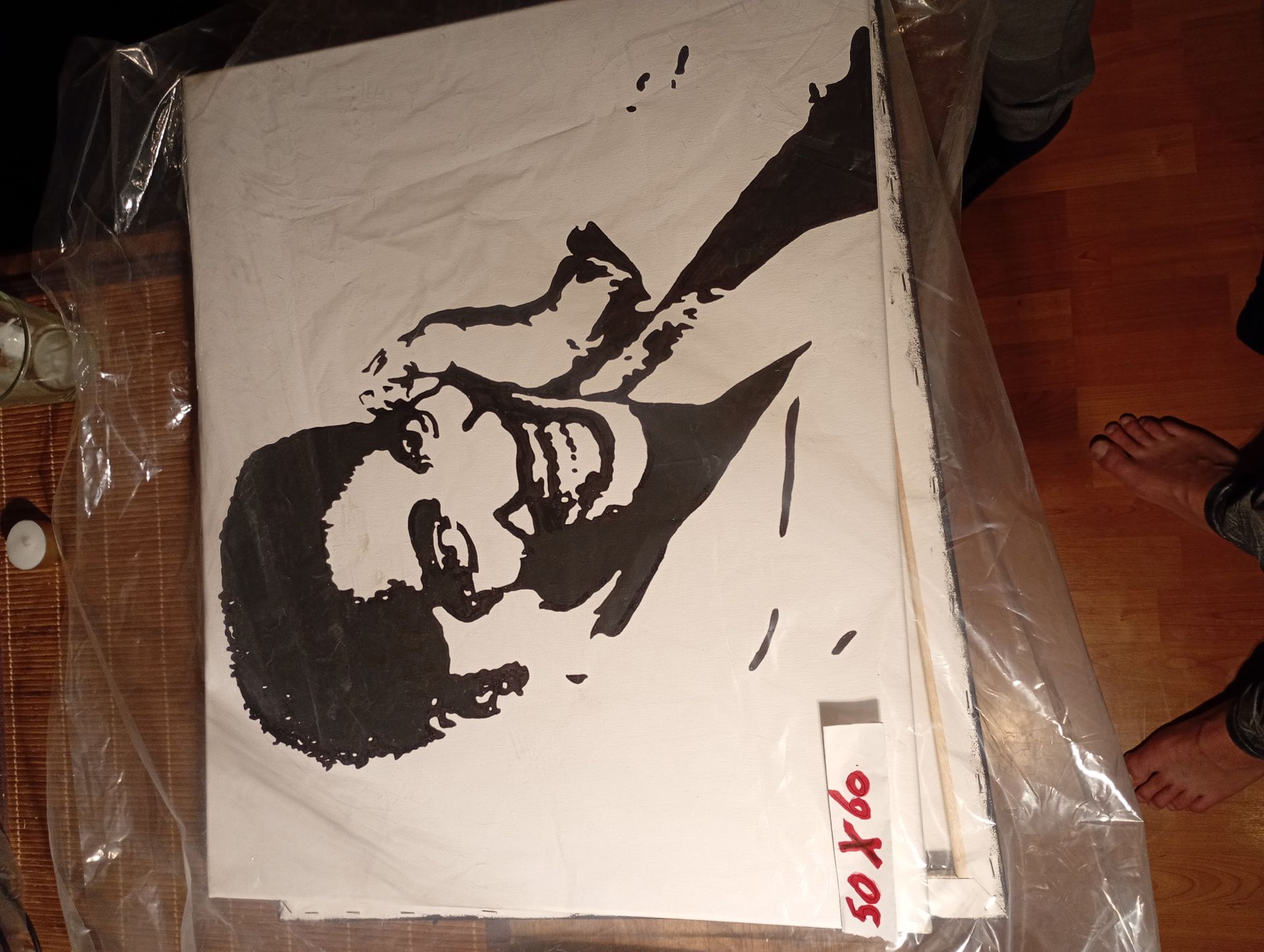Zwart-wit stencilkunst van een gezicht met handen die het hoofd bedekken. De kunst is gestapeld met andere werken.