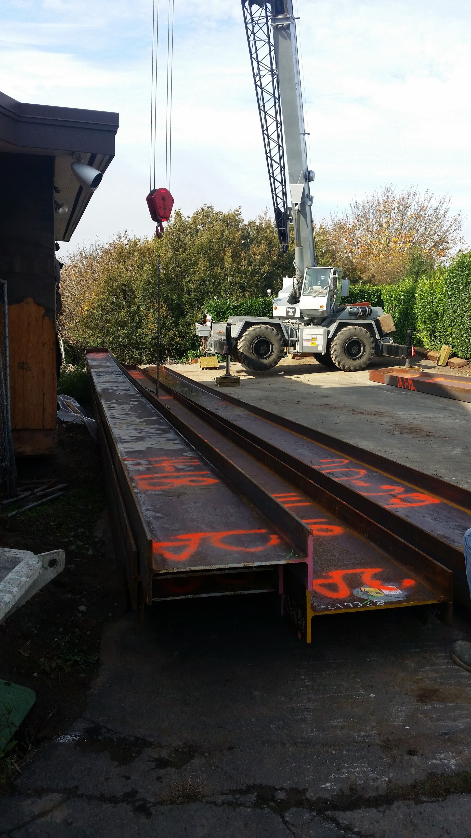 A crane is lifting a large piece of metal in front of a house.