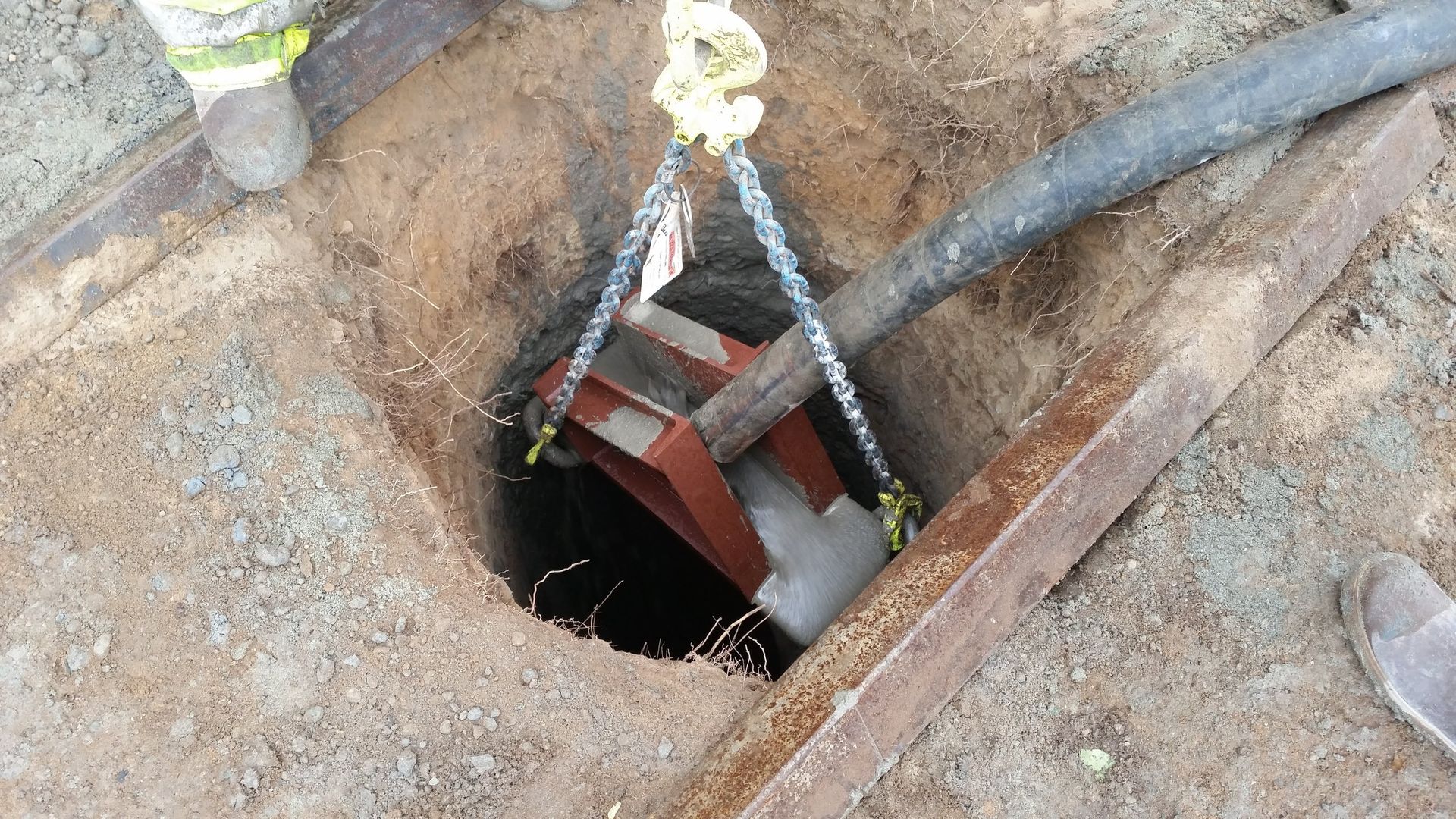 A person is lifting a pipe out of a hole in the ground.