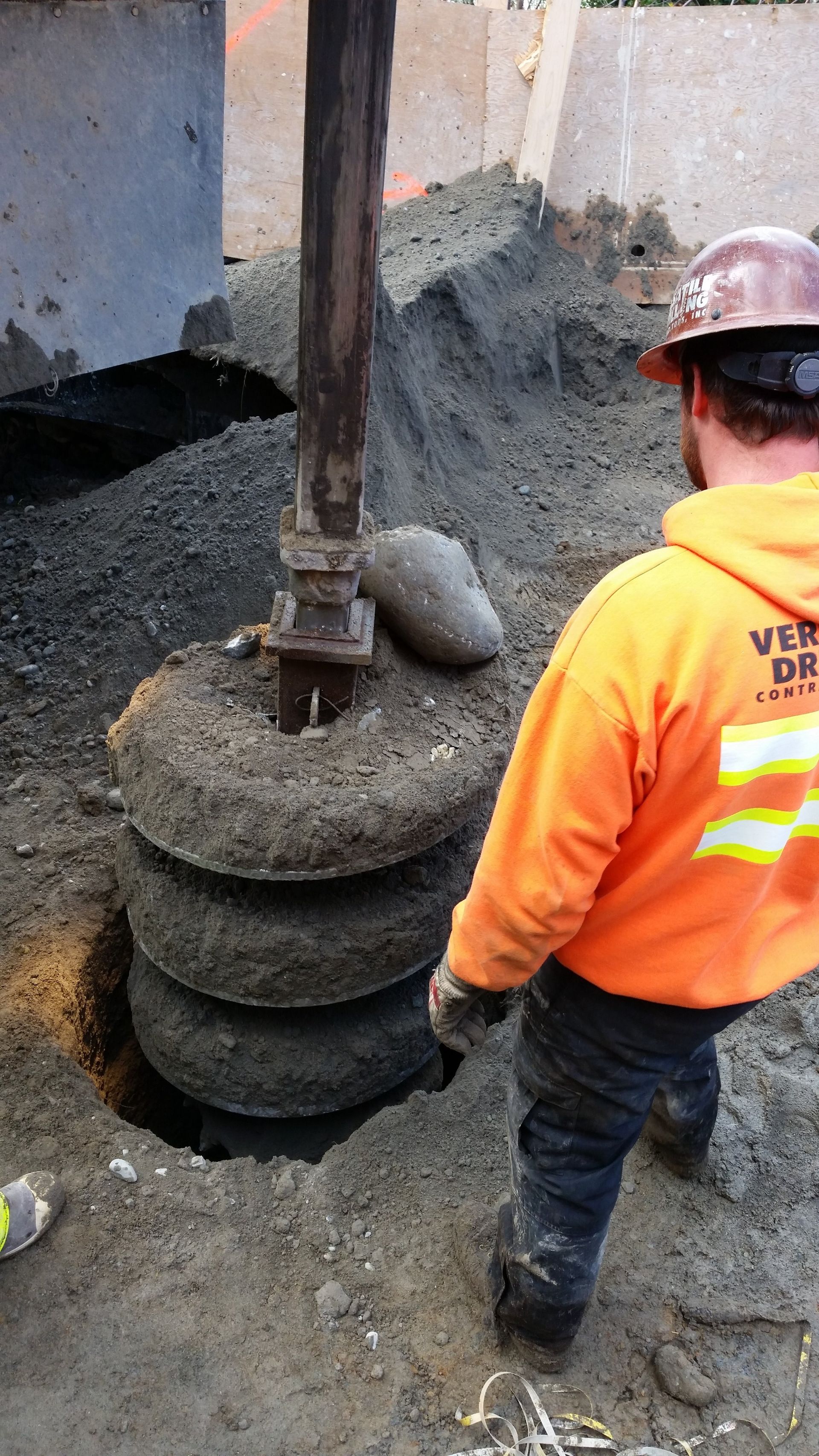 A man wearing a hard hat and an orange hoodie is standing in the dirt.