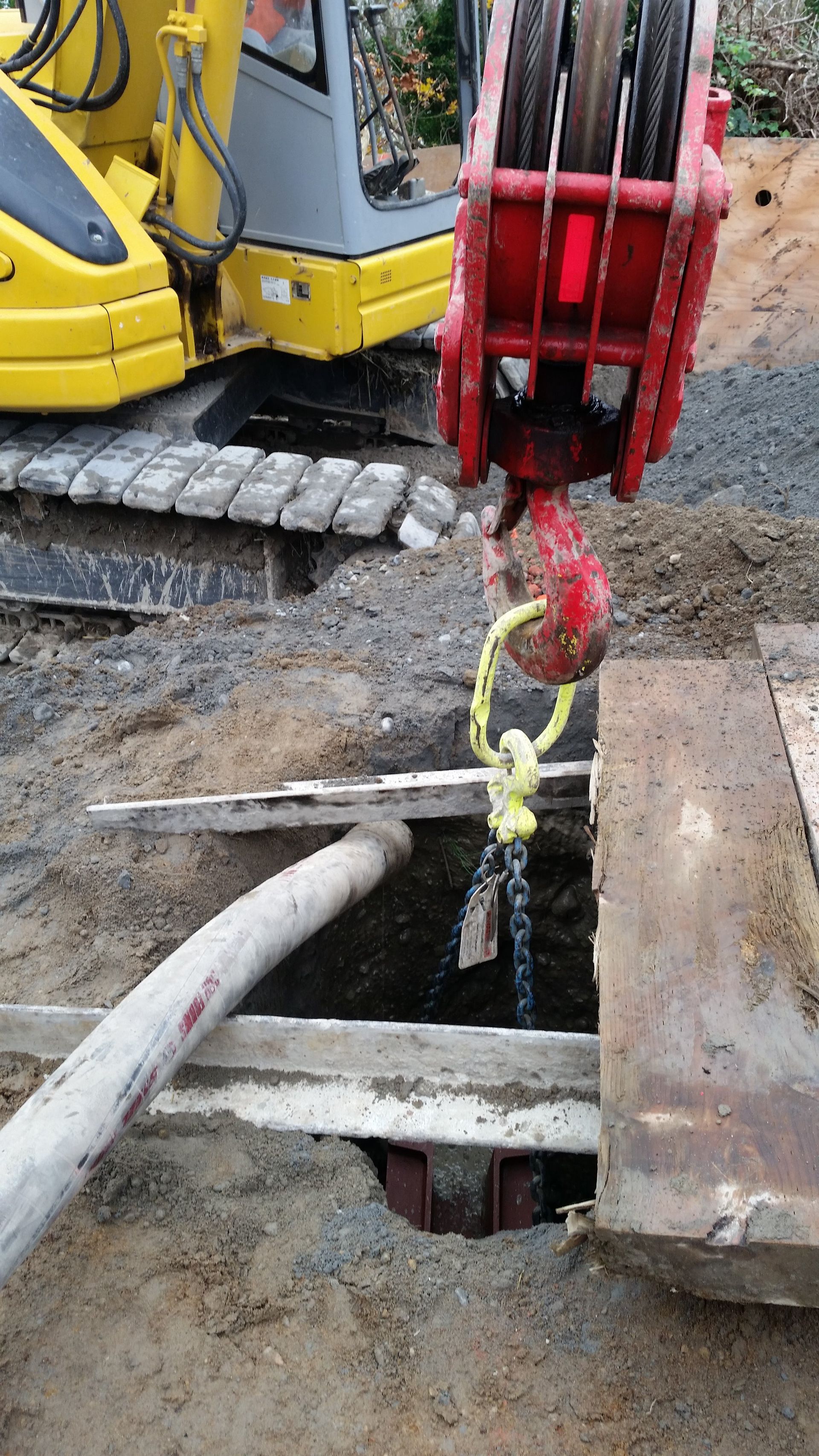 A crane is lifting a hose into a hole in the ground.
