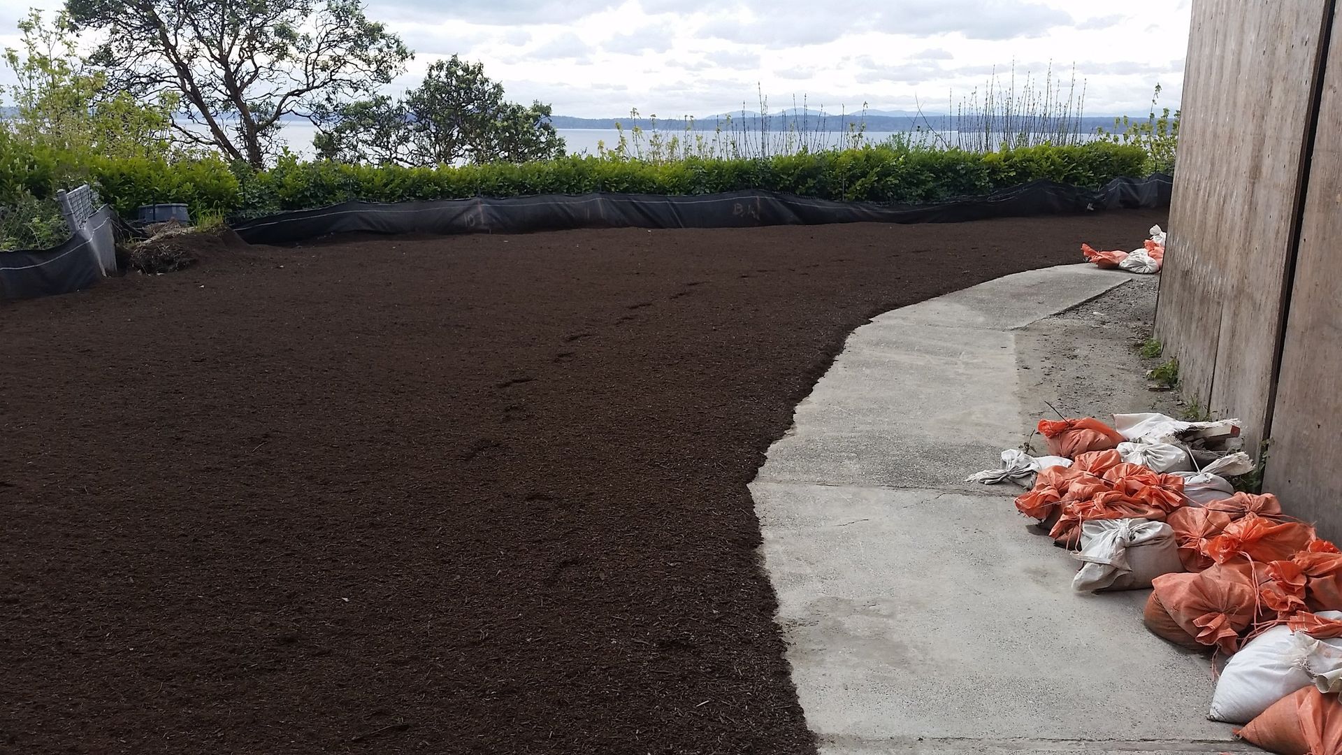 A pile of bags of dirt is sitting on a sidewalk next to a building.