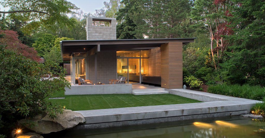 A small house with a pond in front of it surrounded by trees.