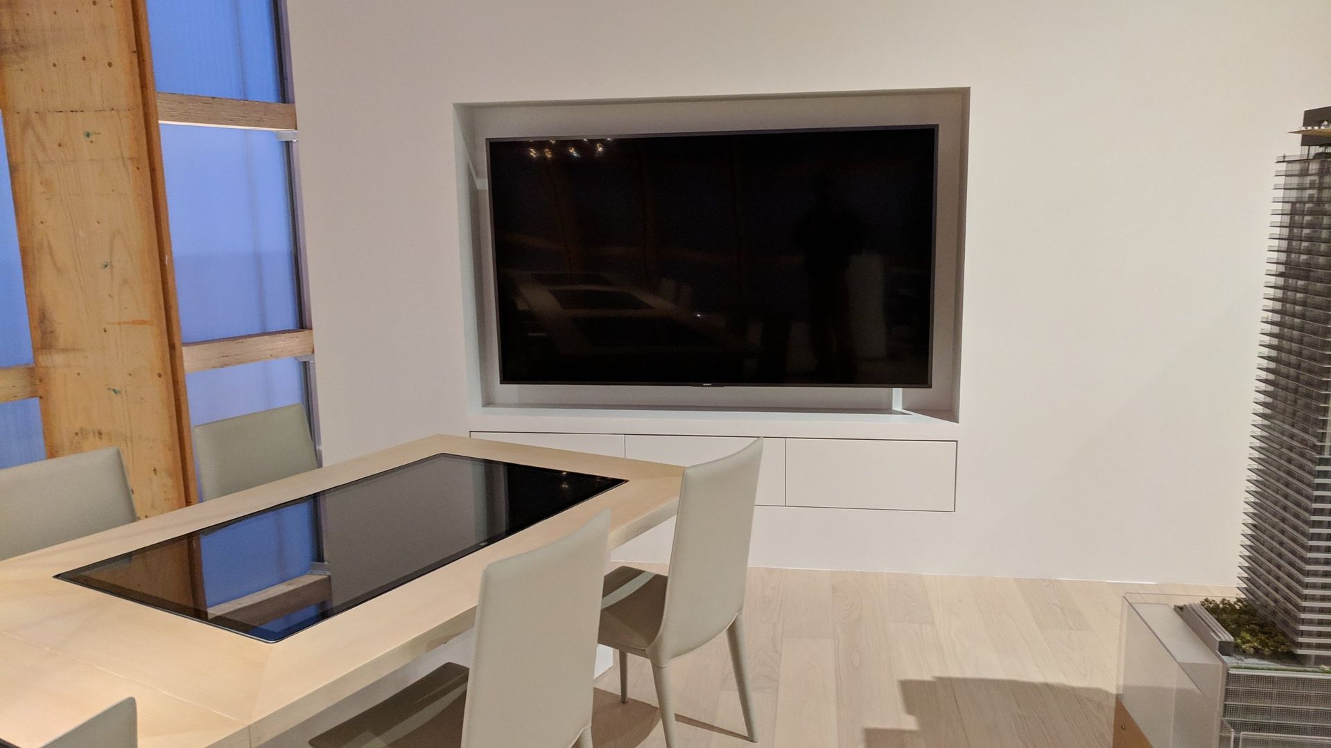 A dining room with a table and chairs and a flat screen tv on the wall.