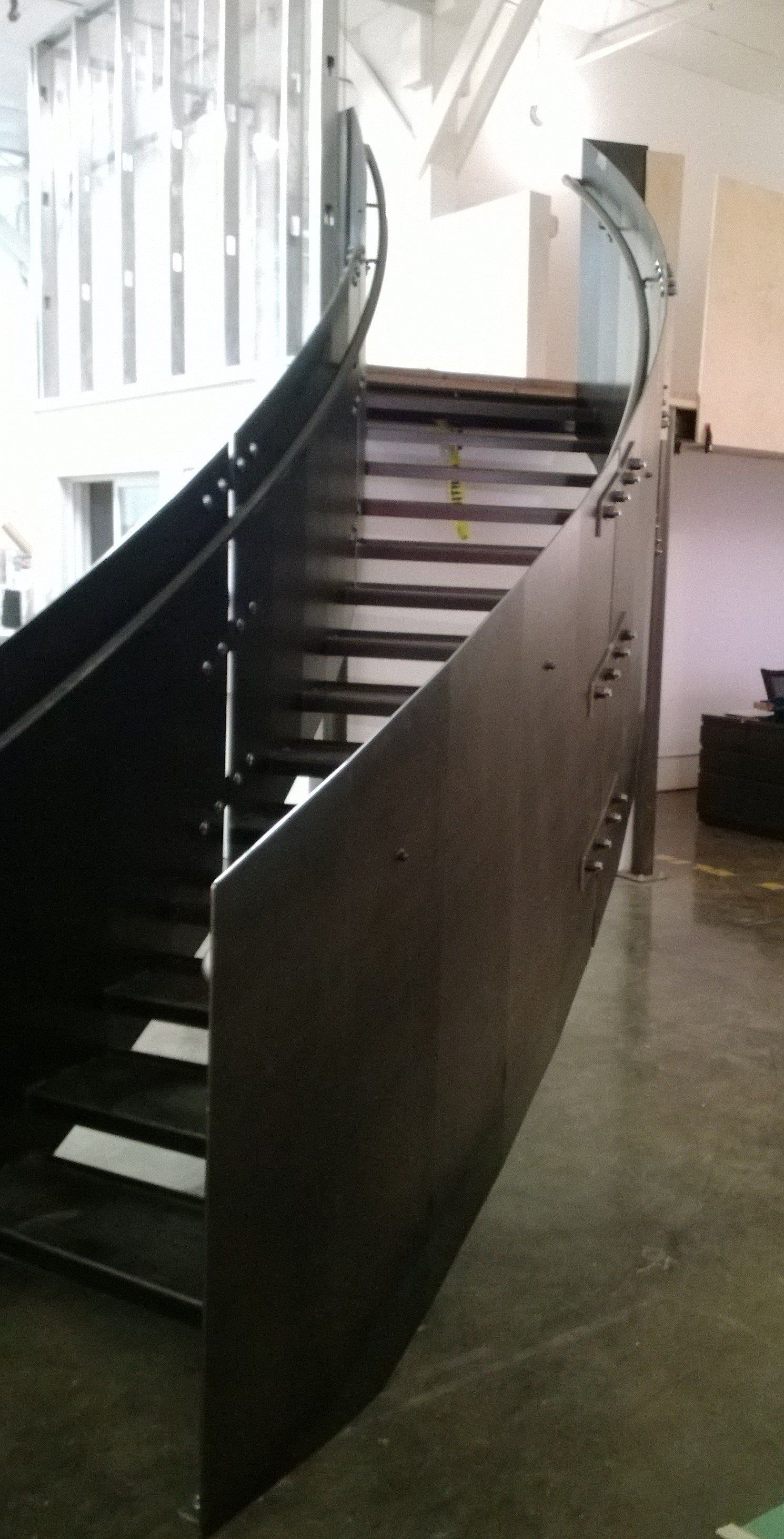 A curved staircase with a glass railing in a room.