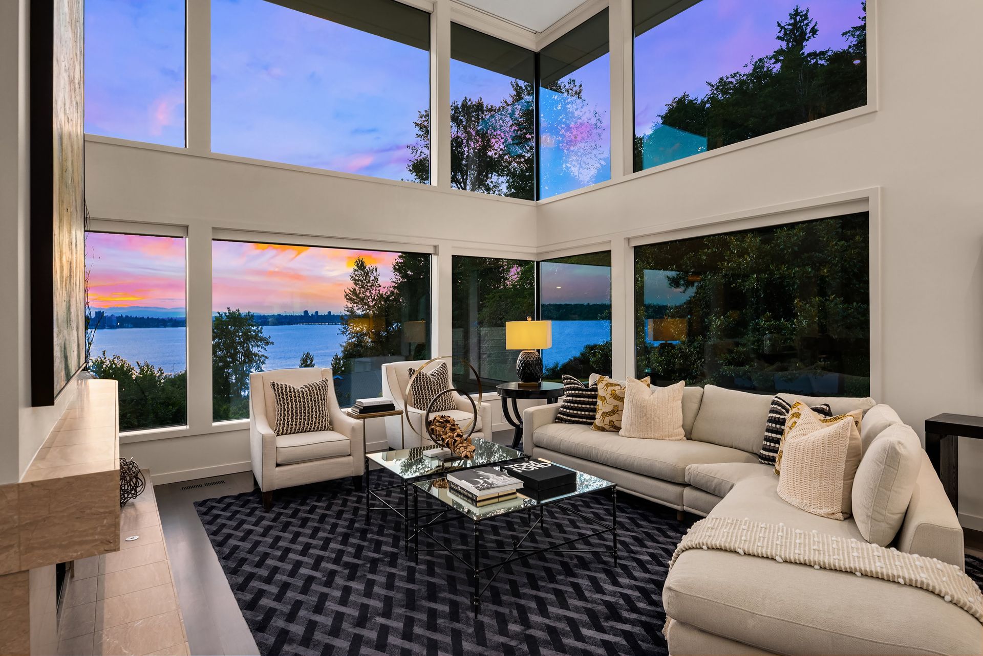 A living room with a couch , chairs , coffee table and lots of windows overlooking a lake.