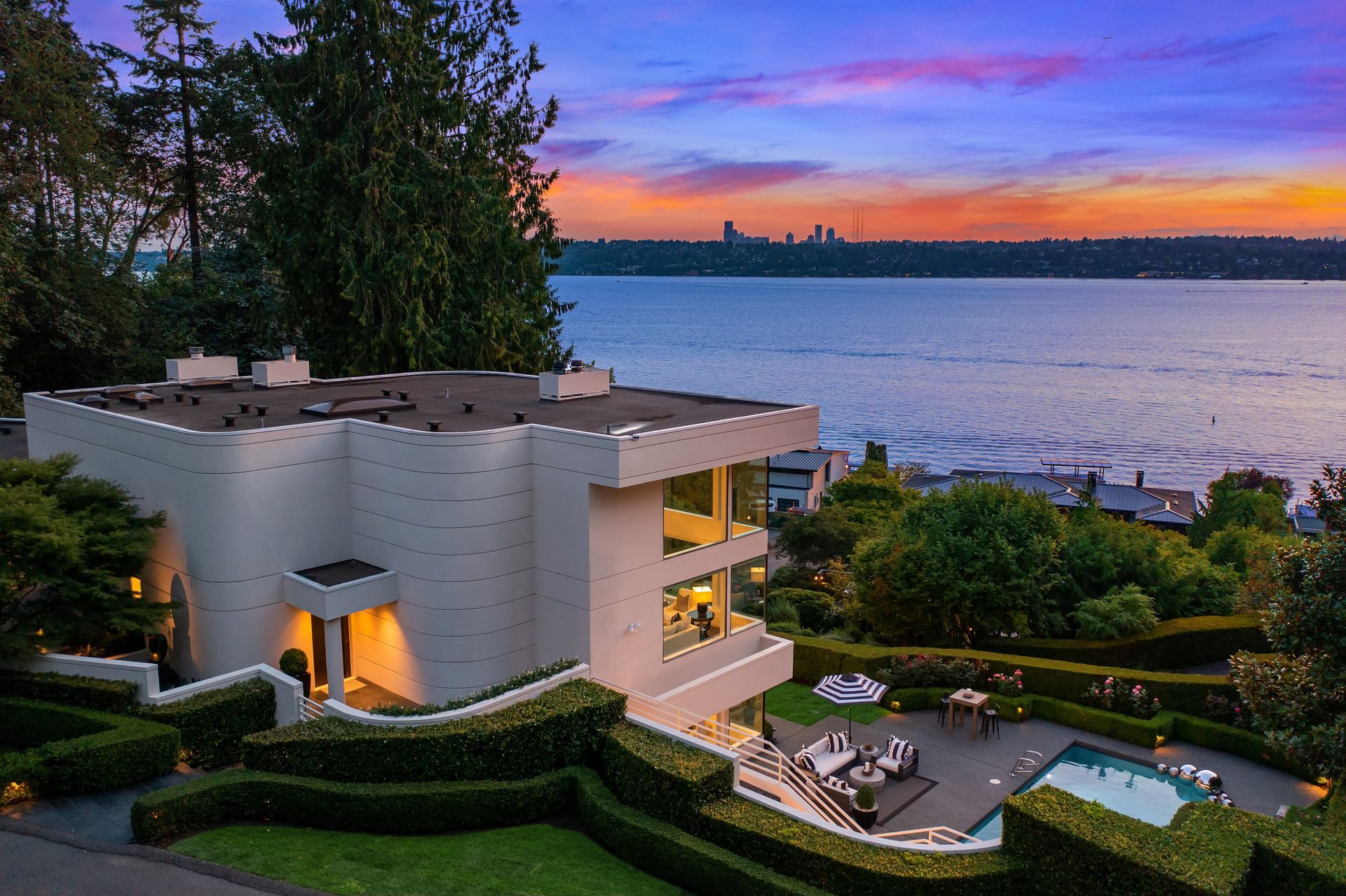 A large white house with a pool in front of a body of water at sunset.
