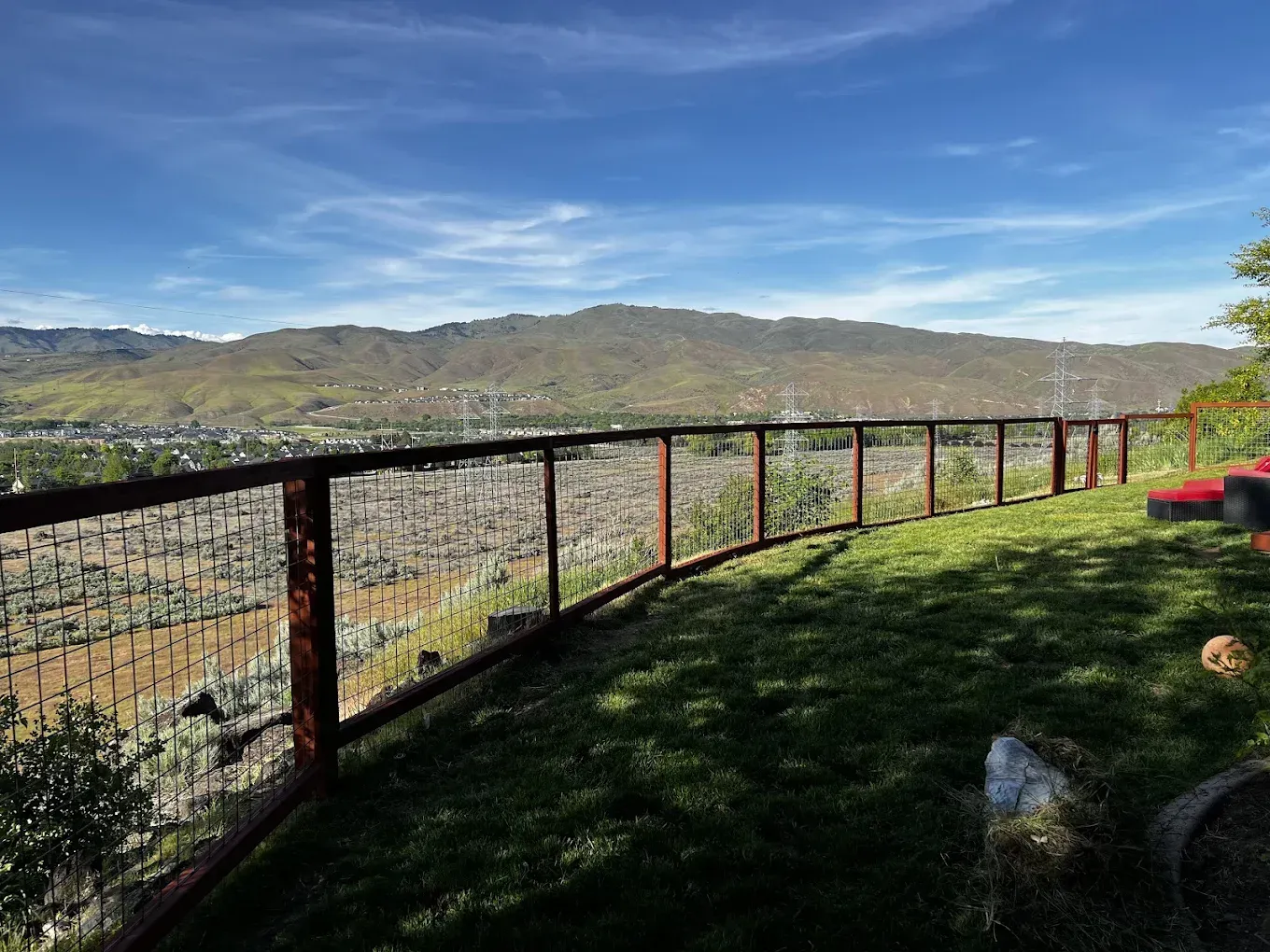 Curved fence overlooking a sunlit valley and distant hills under a blue sky