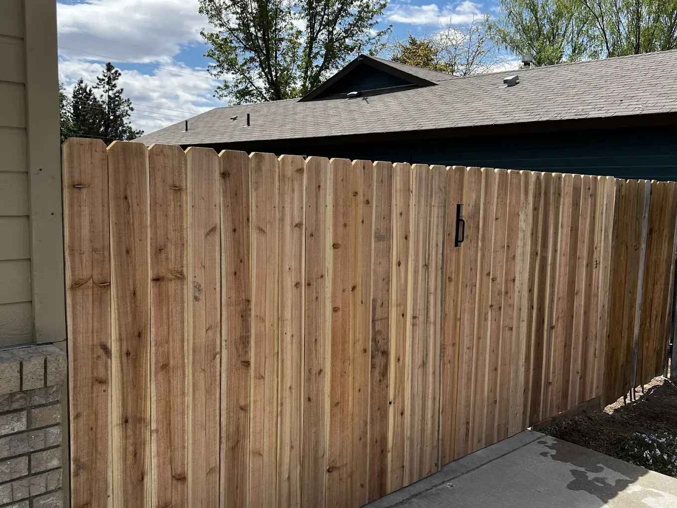 New wooden privacy fence beside a driveway and cinder block wall under a partly cloudy sky