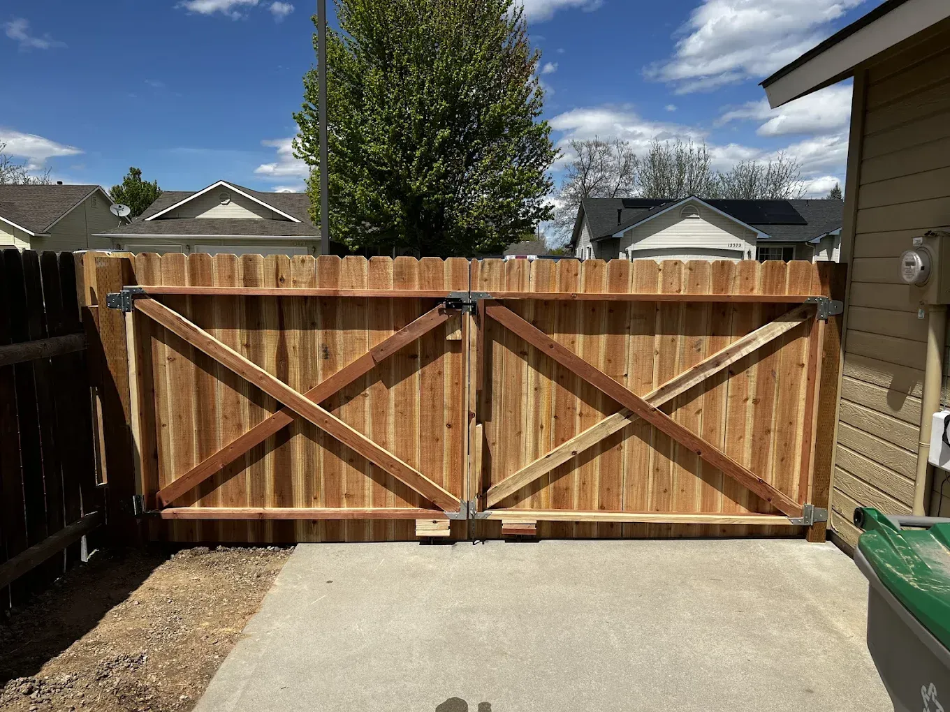 Wooden double gate with X-braces closing off a concrete driveway between a house and fence.