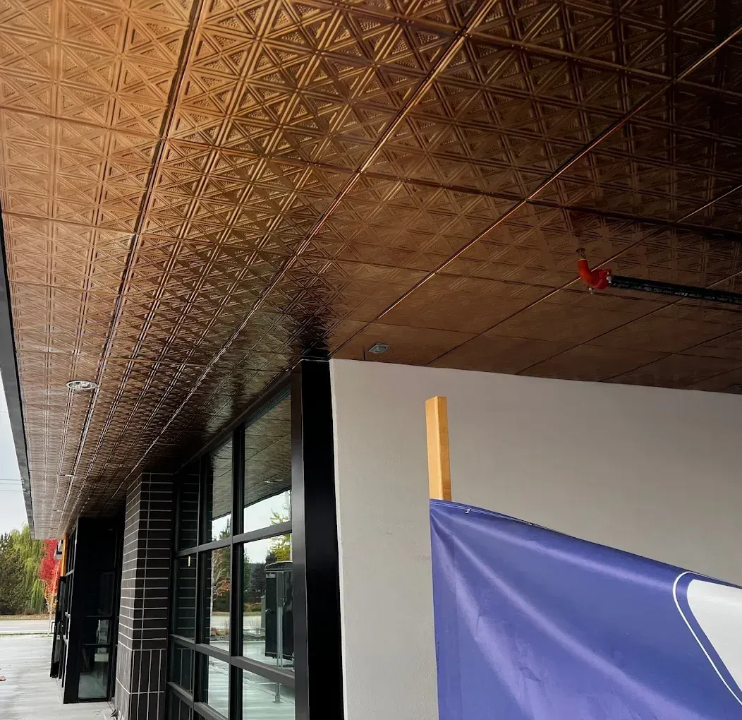 Covered walkway with woven bamboo ceiling, black window frames, and a blue flag along a white wall.
