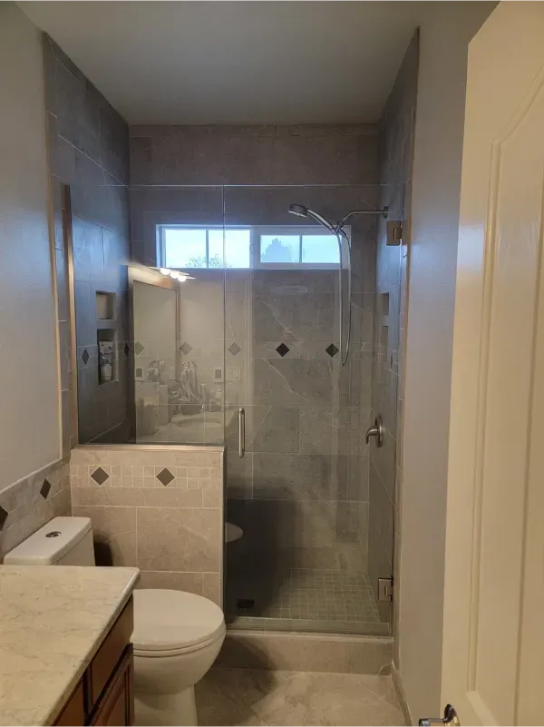 Narrow bathroom with toilet, shower stall, and small window above the shower.