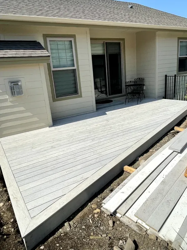 Raised white wooden ramp leading to a house patio door, with railing and deck boards nearby.