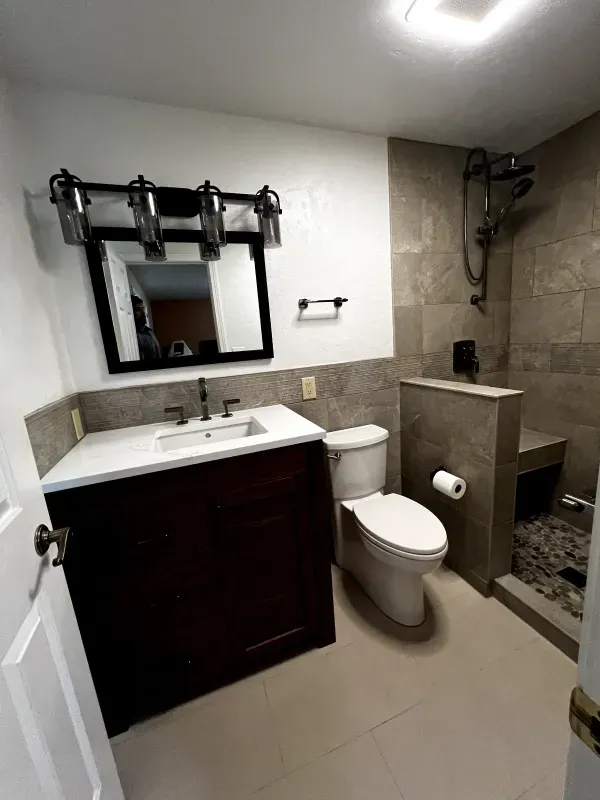 Modern bathroom with vanity, mirror, toilet, and tiled walk-in shower separator