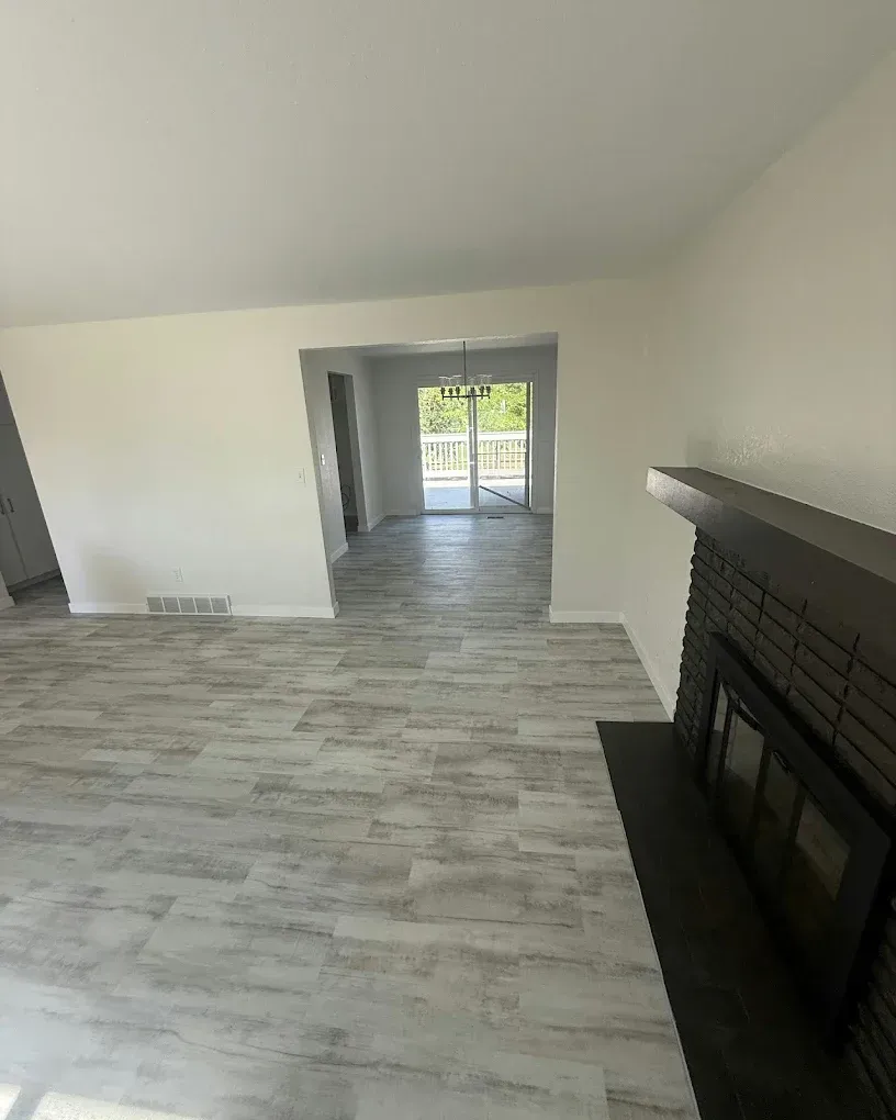 Empty living room with gray wood-look floor, black fireplace, and bright sliding glass doors in back