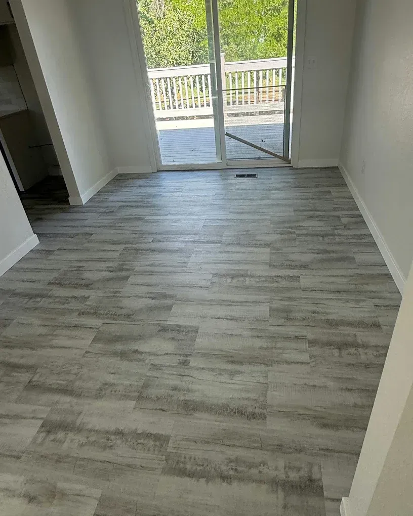 Empty room with gray wood-look flooring and sliding glass doors to a balcony.