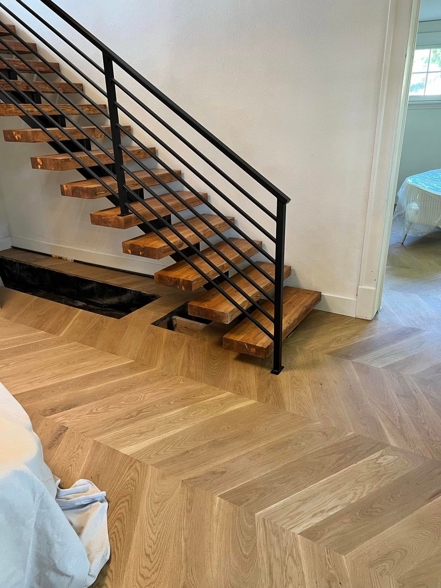 Indoor staircase with black metal railing and wooden herringbone floor in a bright room