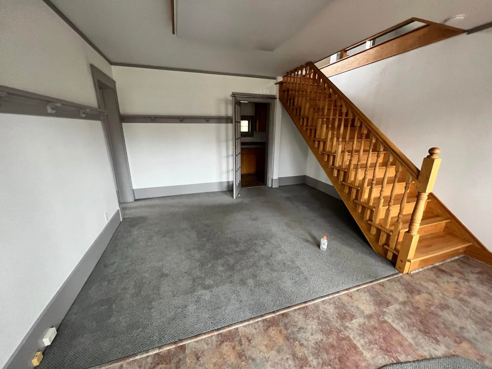 Empty room with gray carpet and a wooden staircase along the right wall.