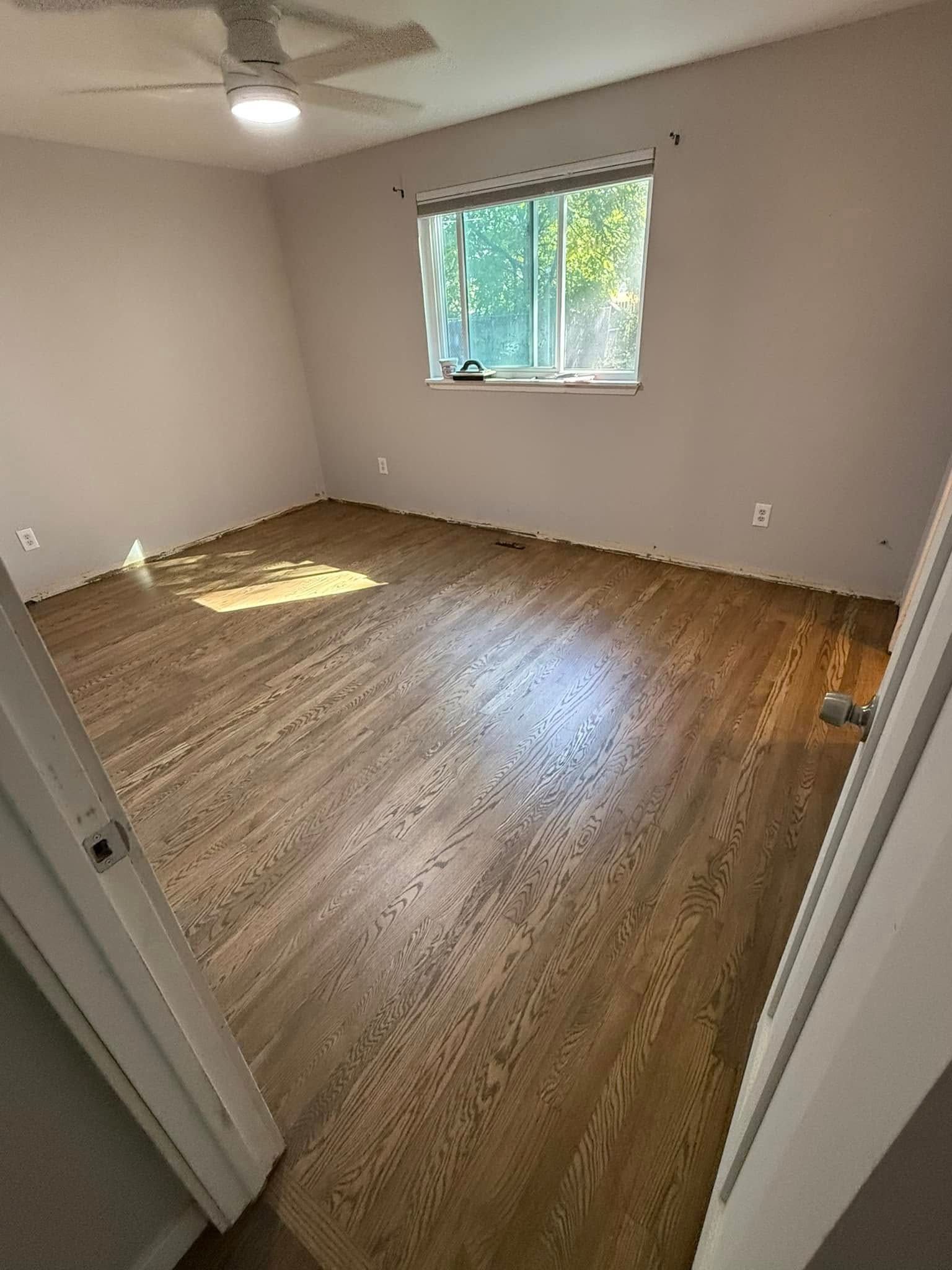 Empty carpeted bedroom with white walls, a ceiling fan, and a small window letting in daylight.
