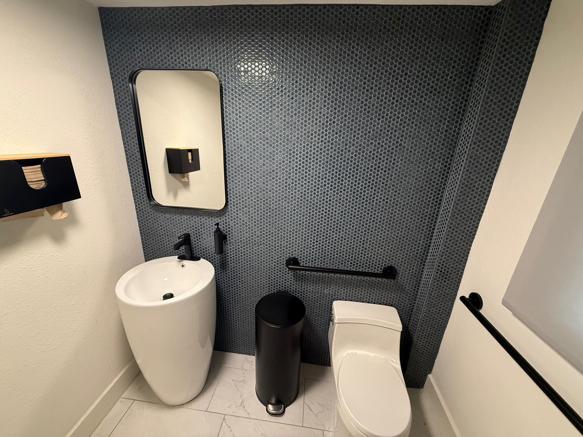 Compact restroom with white toilet, pedestal sink, trash can, and blue textured accent wall