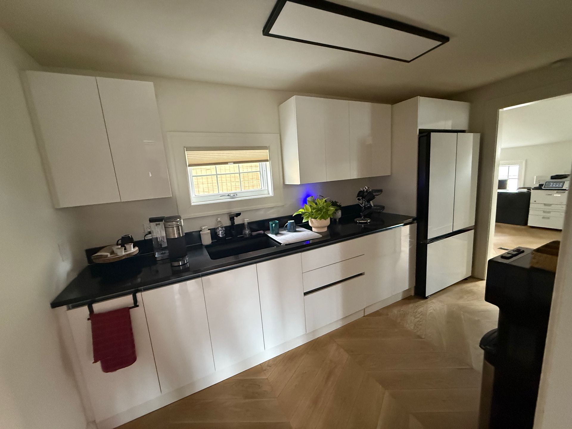 Bright white kitchen with black countertops, stainless fridge, and wood flooring.