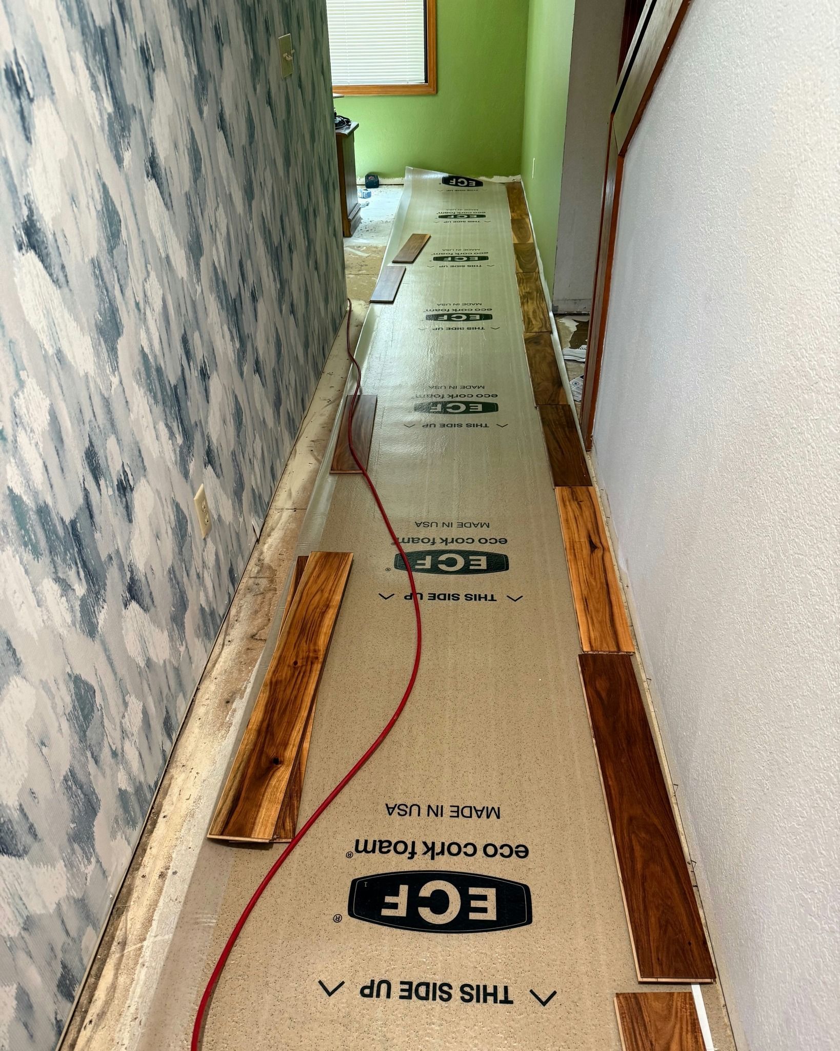 Narrow hallway with flooring underlayment, measuring tape, and tools laid along the floor during renovation
