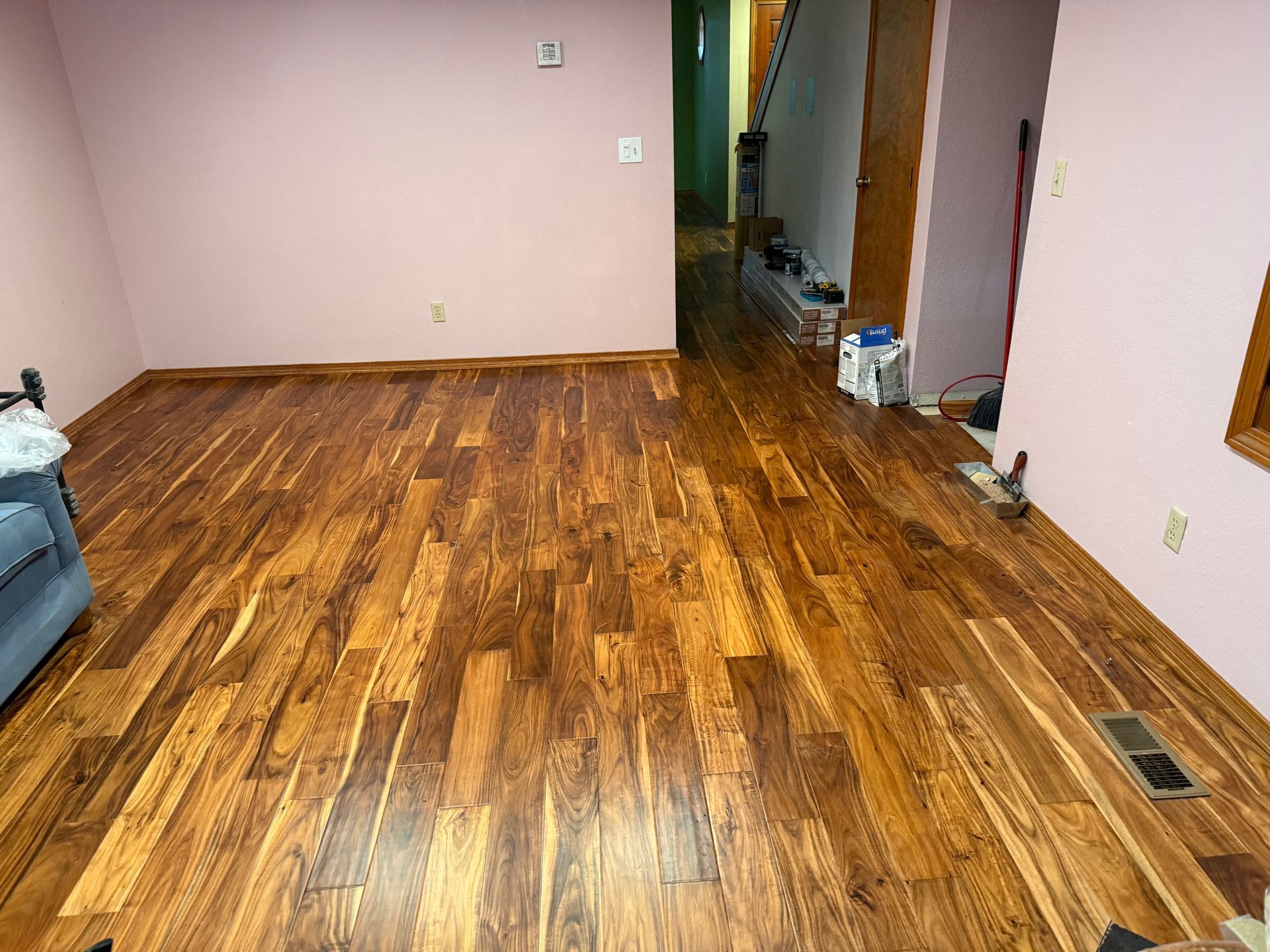 Empty living room with wood floors, pale walls, and a doorway to a hall