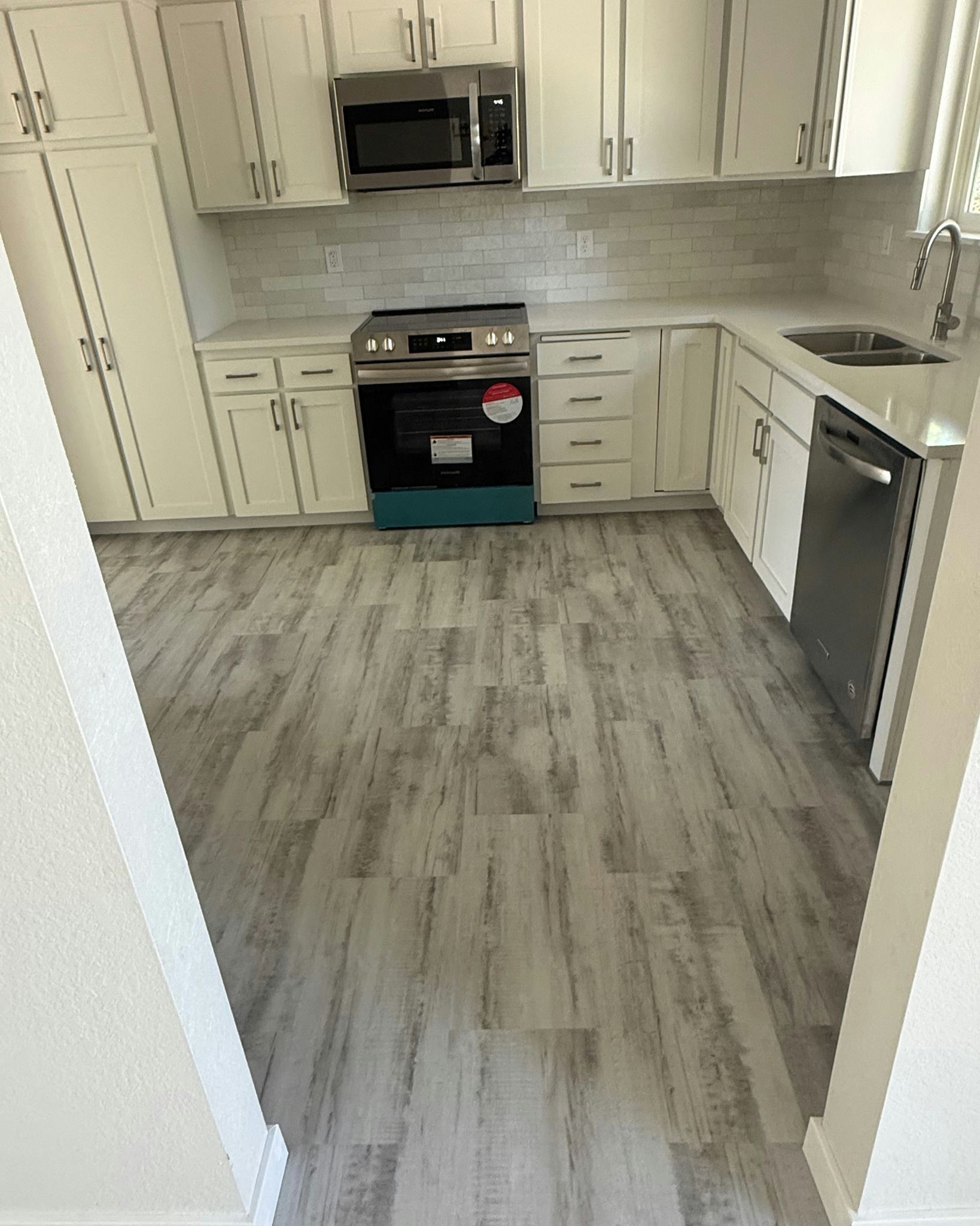 Bright kitchen with white cabinets, stainless appliances, and gray wood-look flooring