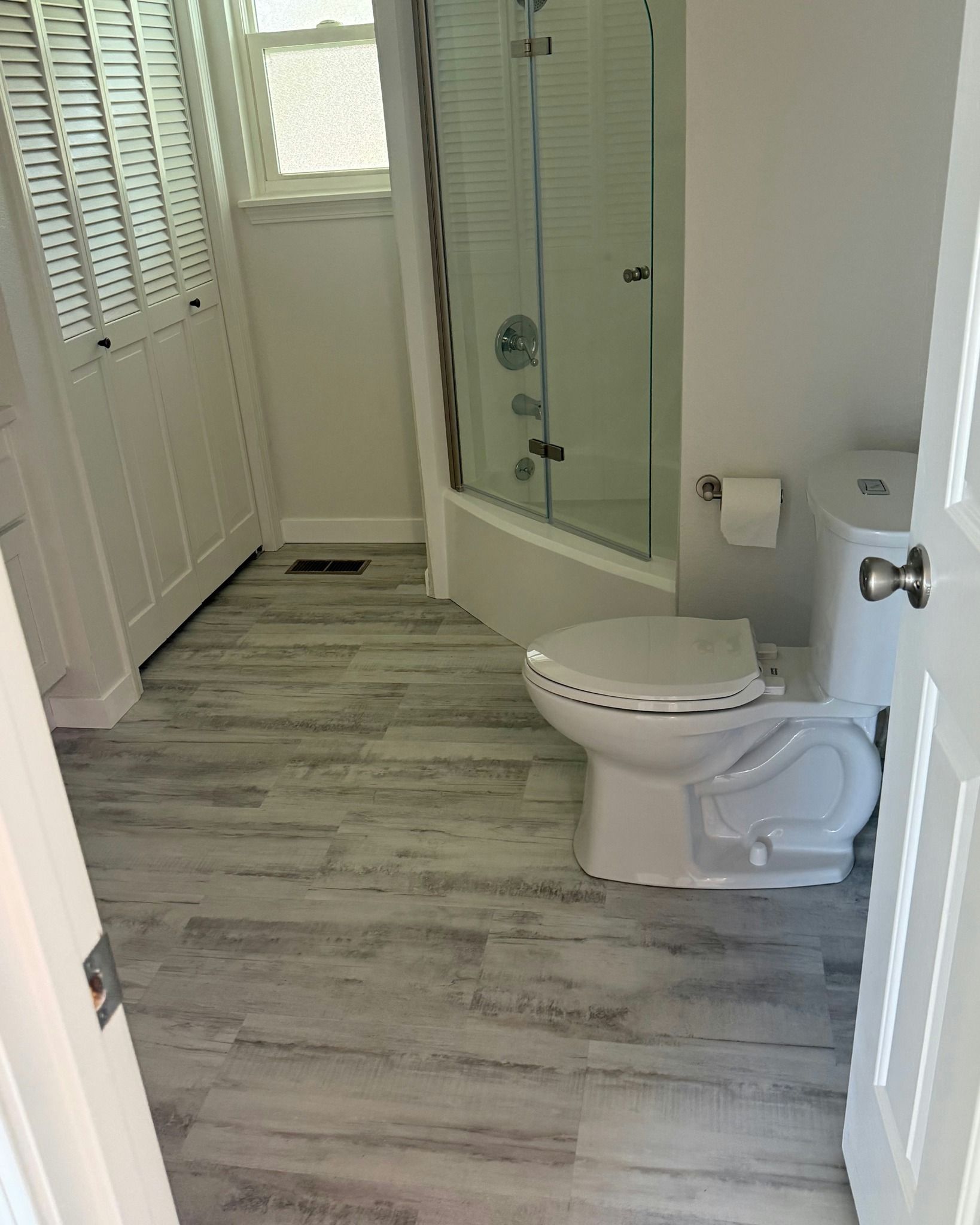 Small bathroom with a toilet, glass shower, and gray wood-look flooring.