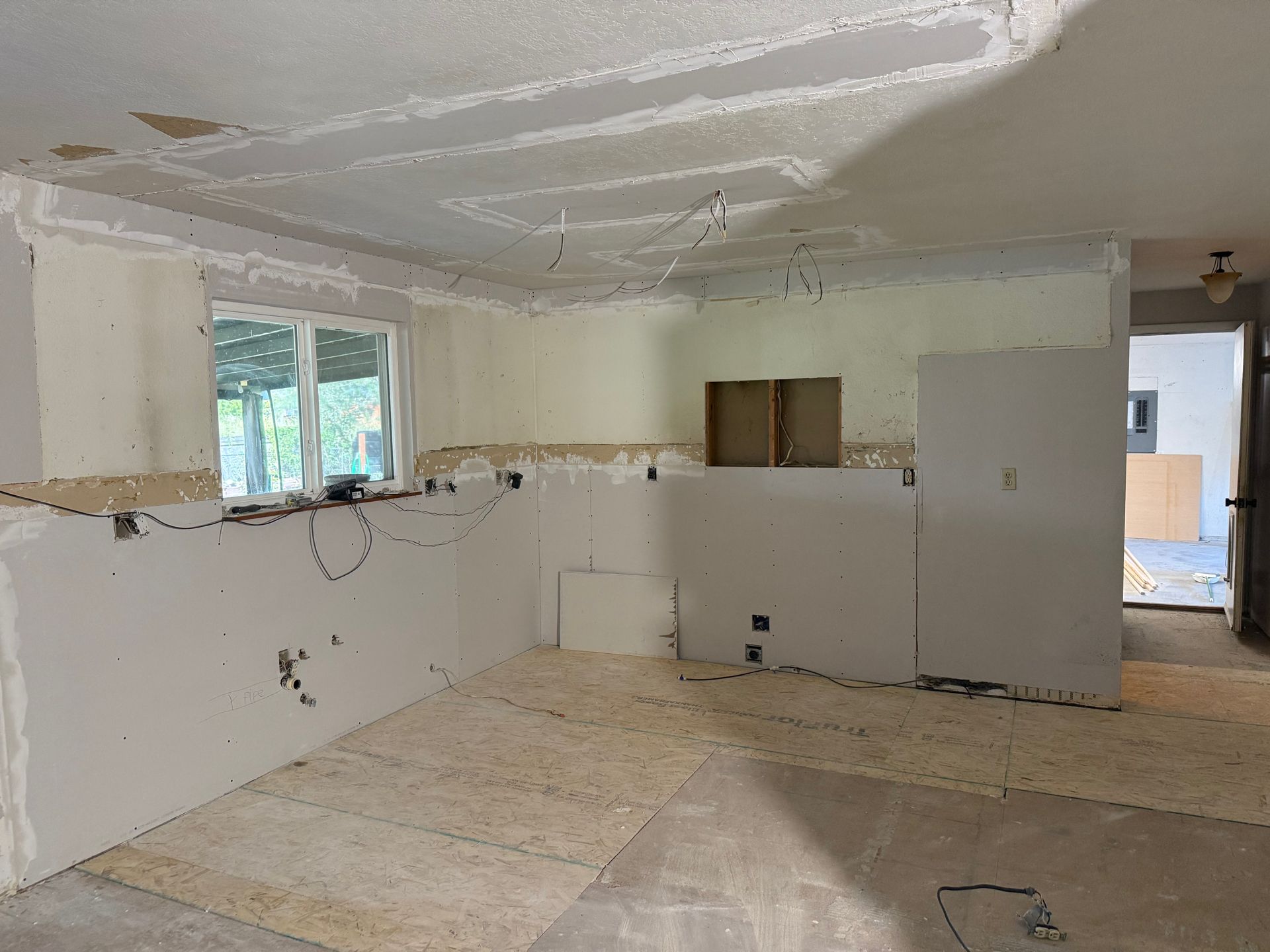 Partially renovated kitchen with white drywall, exposed seams, and unfinished floor panels