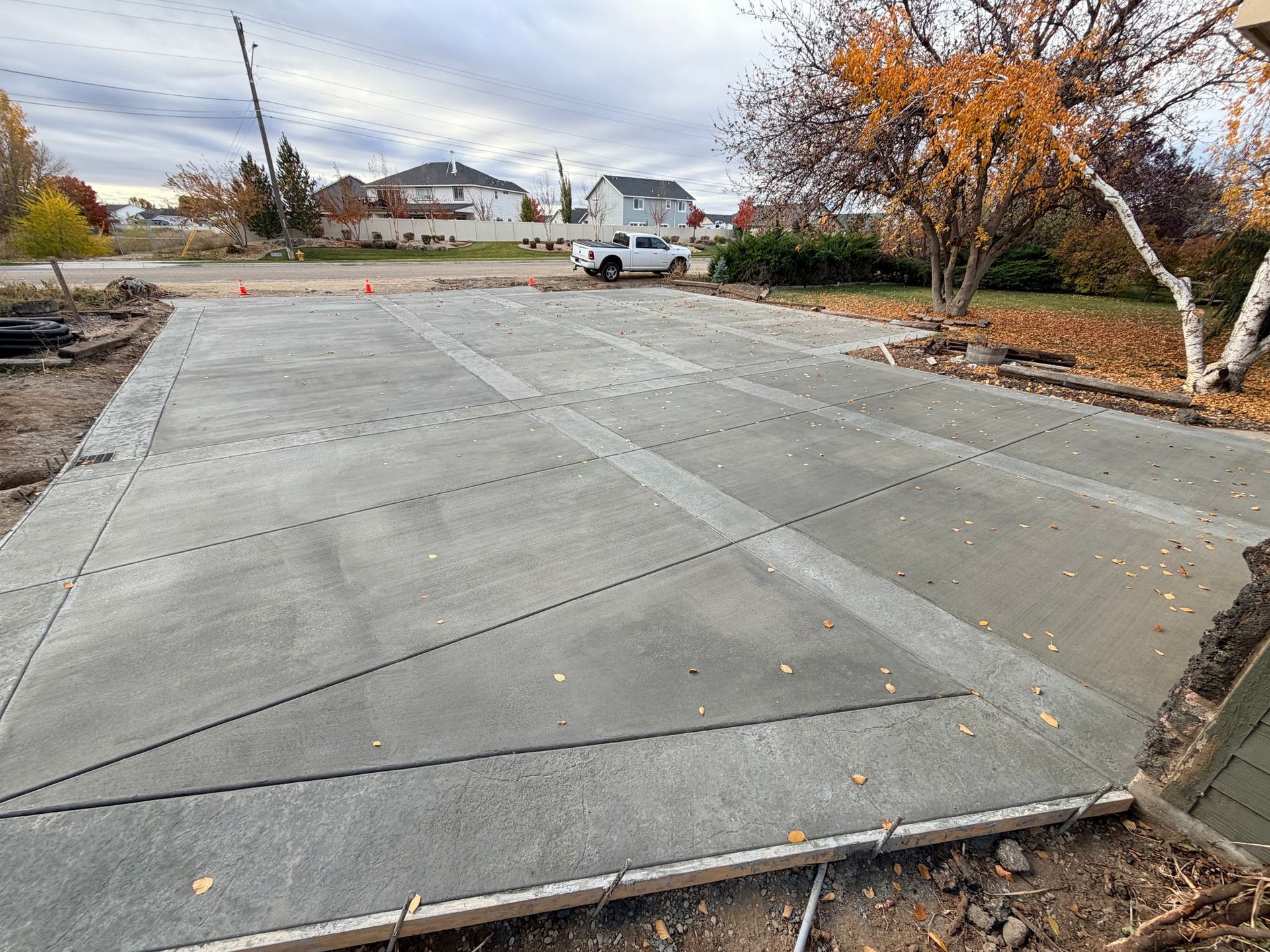 Empty concrete driveway beside autumn trees and a parked white pickup truck under cloudy skies