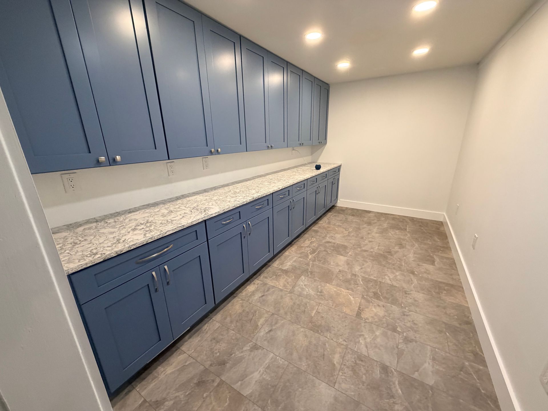 Blue cabinets and granite counters in a bright empty room with gray tile flooring.