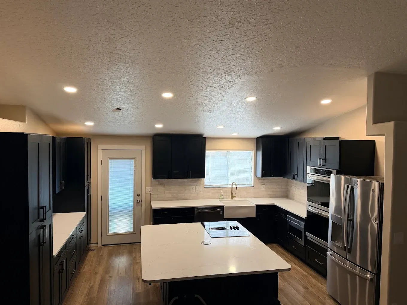 Modern kitchen with dark cabinets, white island, stainless steel appliances, and recessed lighting