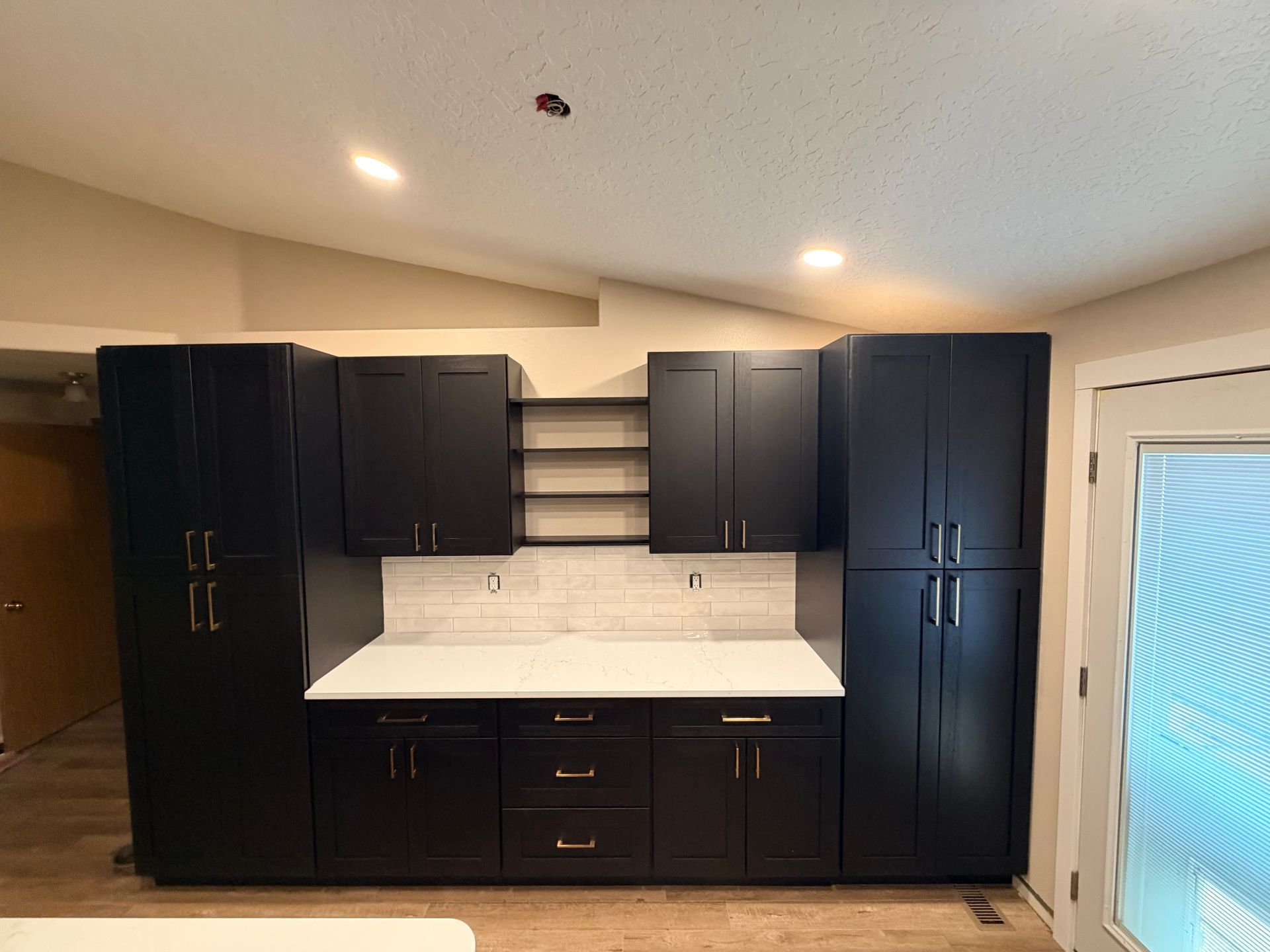 Dark navy kitchen cabinets with white countertop and tile backsplash in a bright room