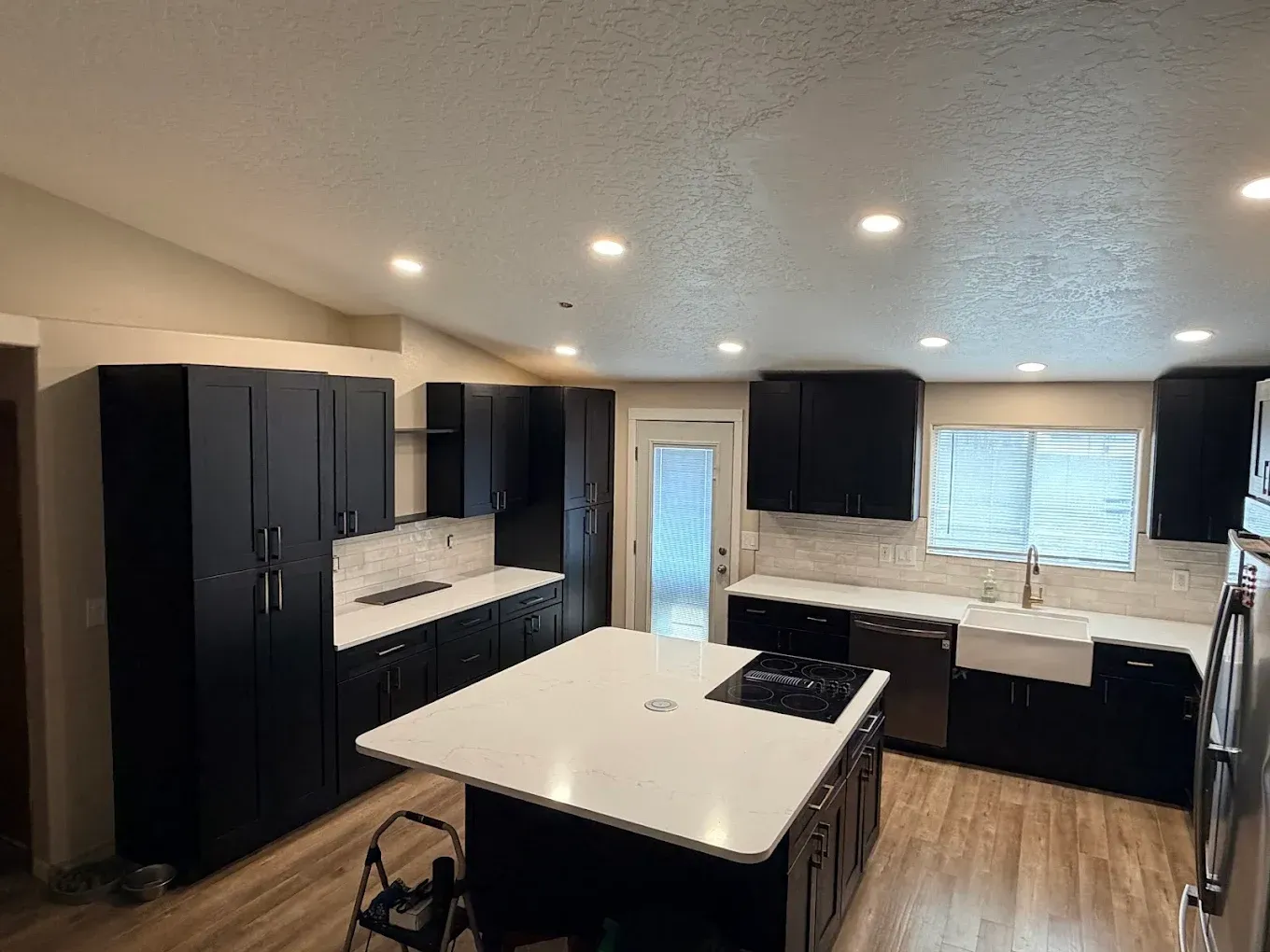 Modern kitchen with black cabinets, white island, stainless stove, and wood floors