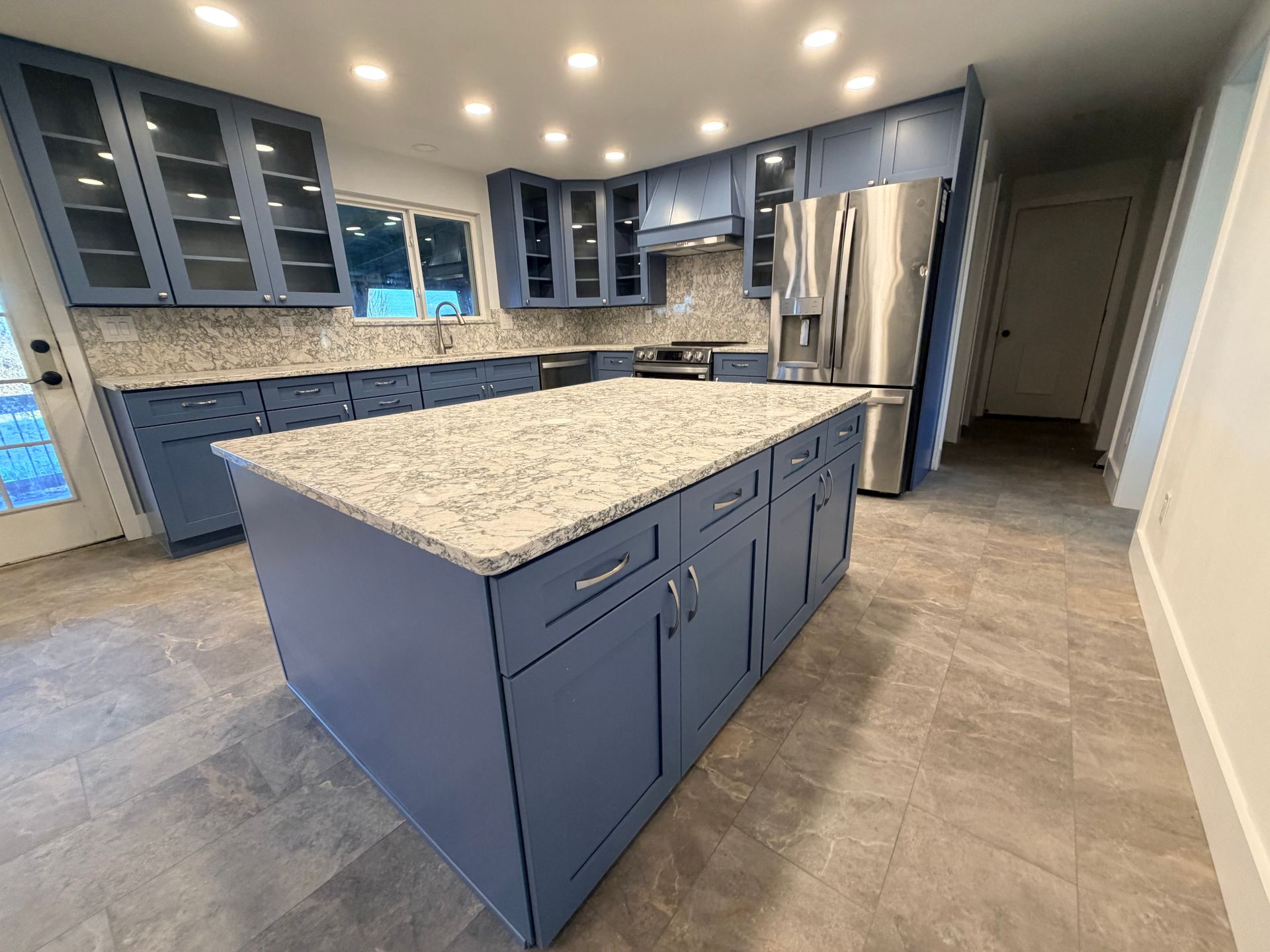 Modern kitchen with blue cabinets, granite island, stainless steel appliances, and recessed lighting